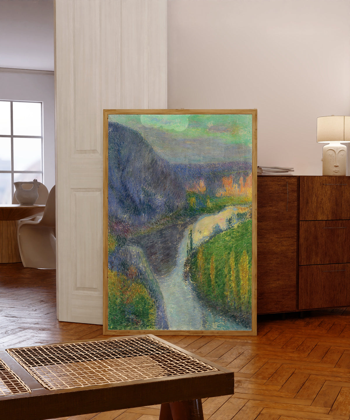 Framed art print of La vallée du Lot, près de Saint-Cirq Lapopie by Henri Martin, in a light wood frame leaning in a warm room with a parquet floor