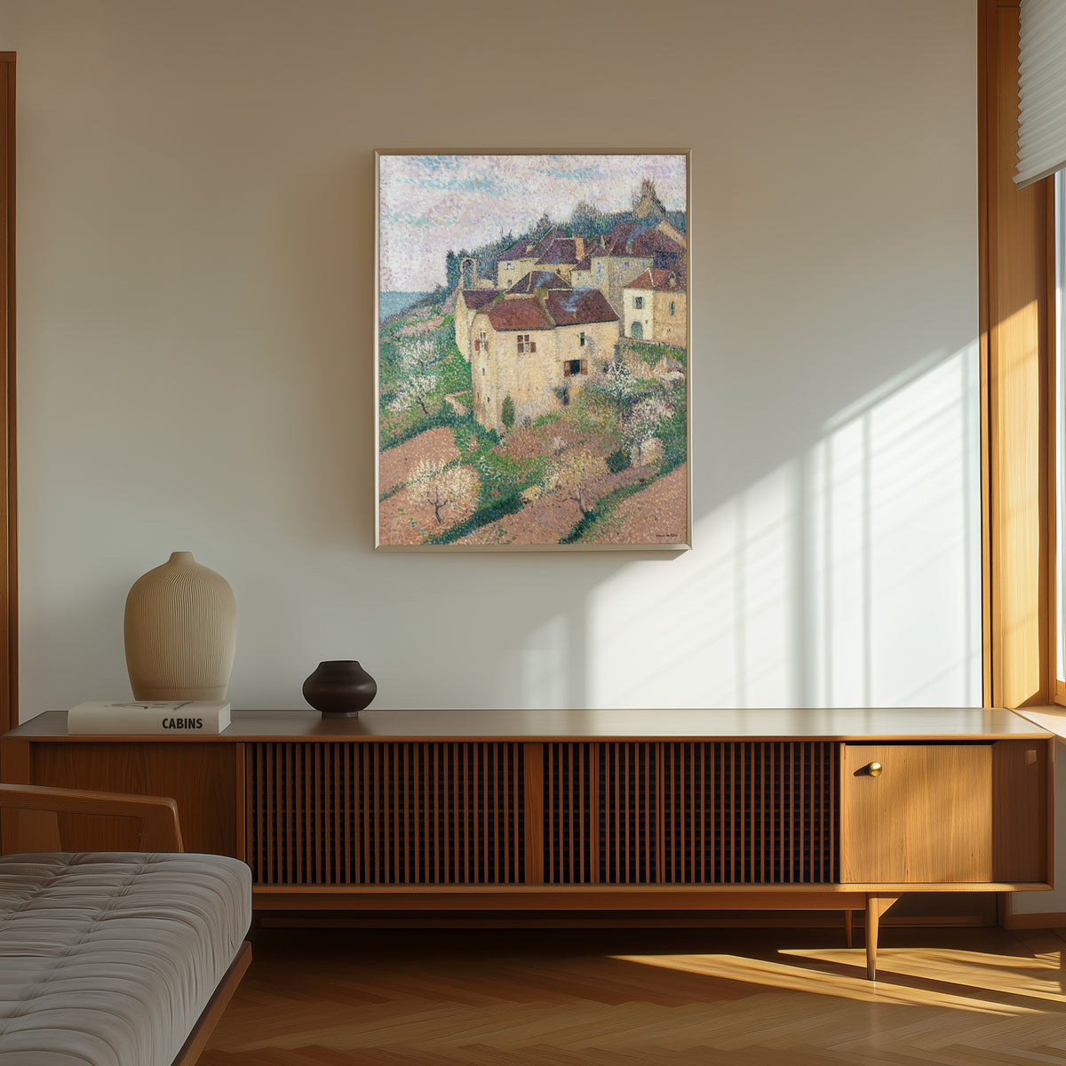 Framed art print of Maisons à Saint-Cirq-Lapopie by Henri Martin, in a thin light frame on a sunlit wall above a wooden sideboard
