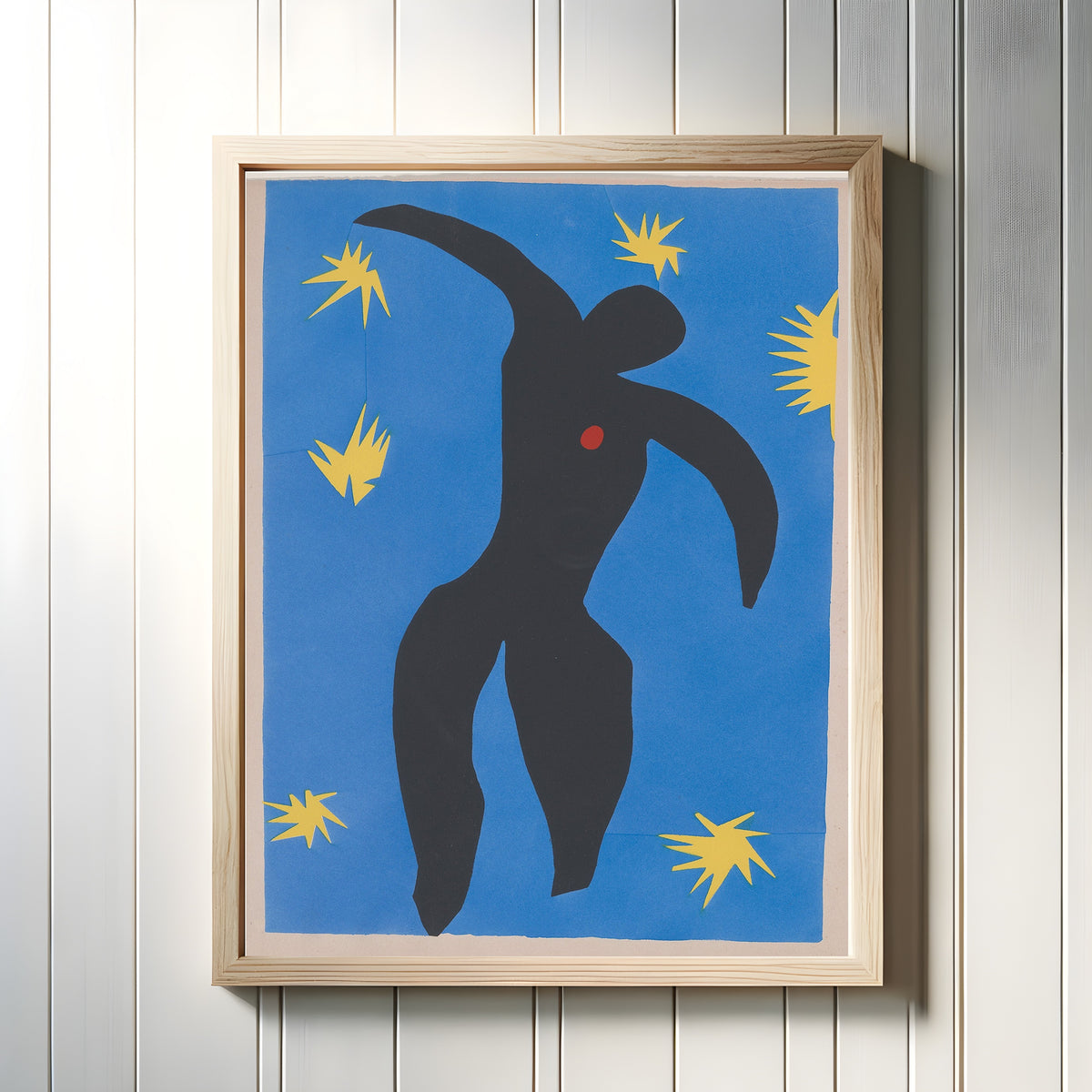 Framed art print of Icarus by Henri Matisse, in a light wood frame on a white panelled wall