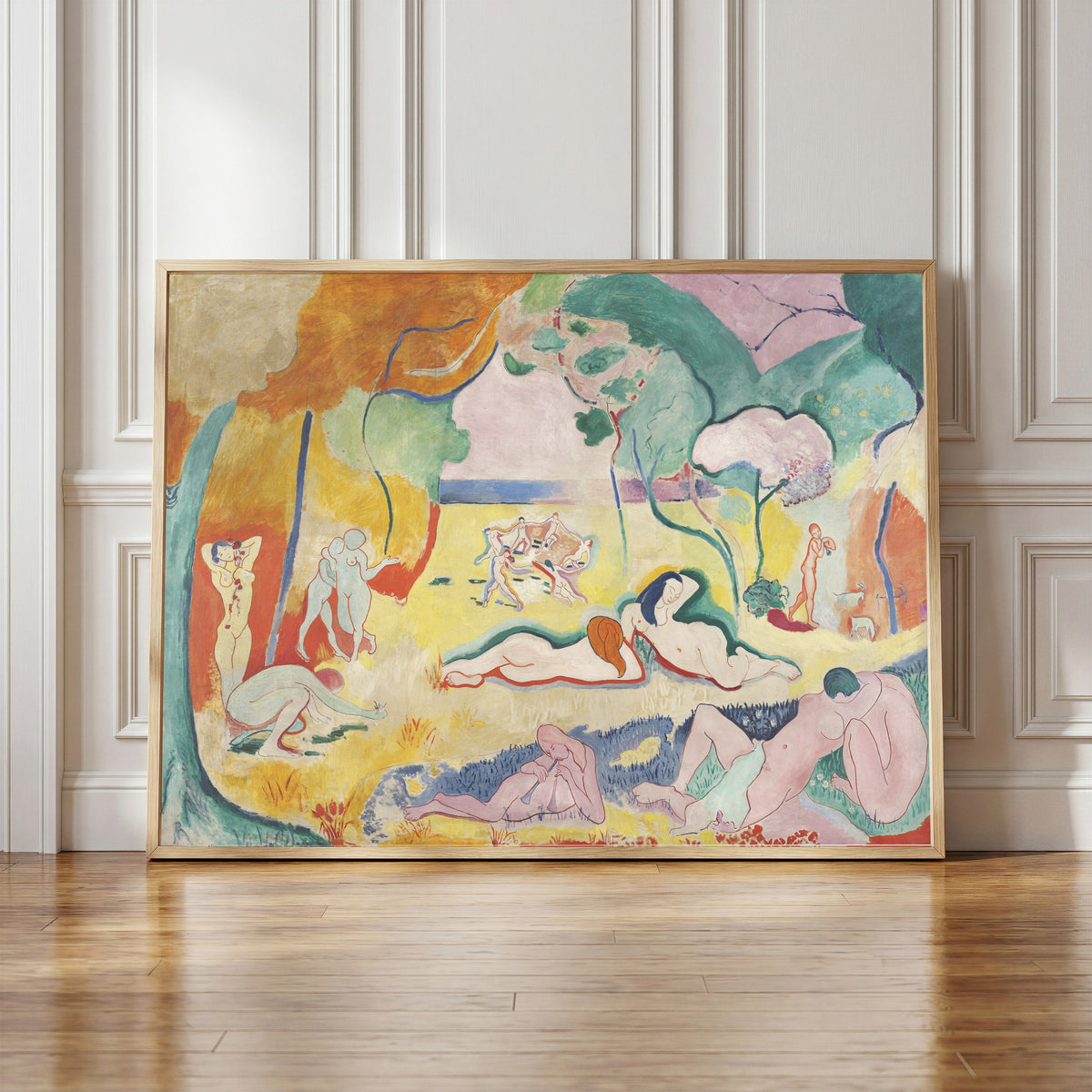 Framed art print of Le Bonheur de vivre (The Joy of Life) by Henri Matisse, in a light wood frame leaning against a panelled white wall