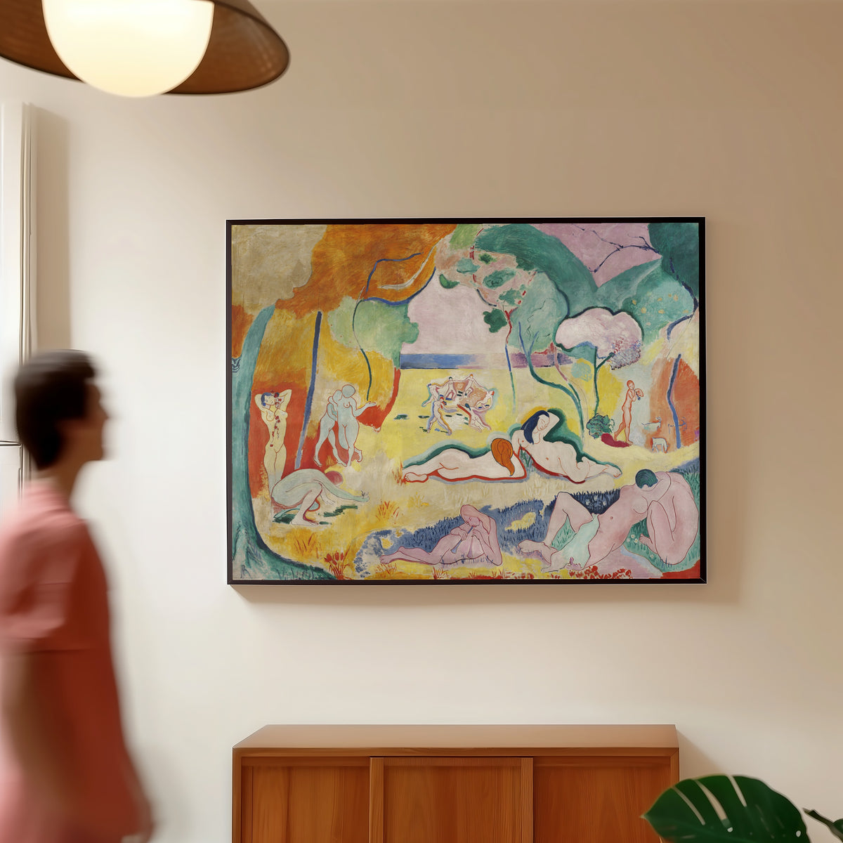 Framed art print of Le Bonheur de vivre (The Joy of Life) by Henri Matisse, in a slim black frame on a warm wall in a sunlit room