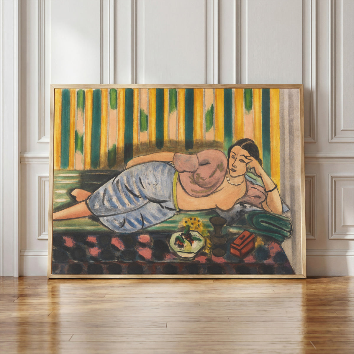 Framed art print of Odalisque with a Red Casket by Henri Matisse, in a light wood frame leaning against a panelled white wall