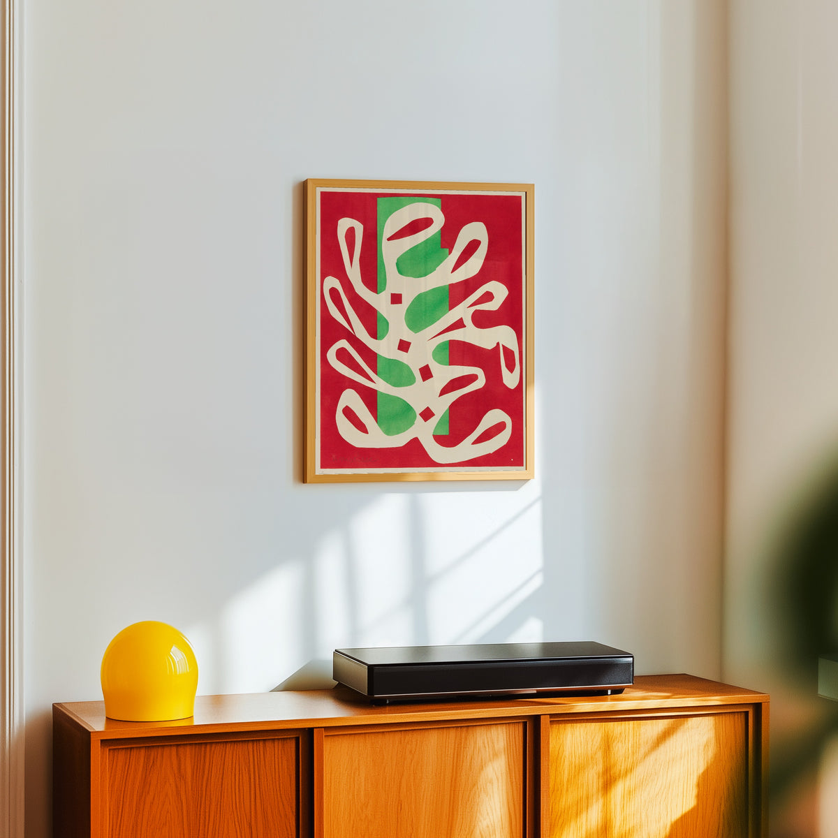 Framed art print of White Algae on Red and Green Ground by Henri Matisse, in a light wood frame on a white wall above an orange sideboard