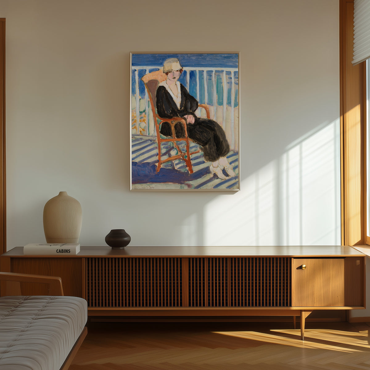 Framed art print of Young Girl on a Balcony over the Ocean by Henri Matisse, in a thin light frame on a sunlit wall above a wooden sideboard