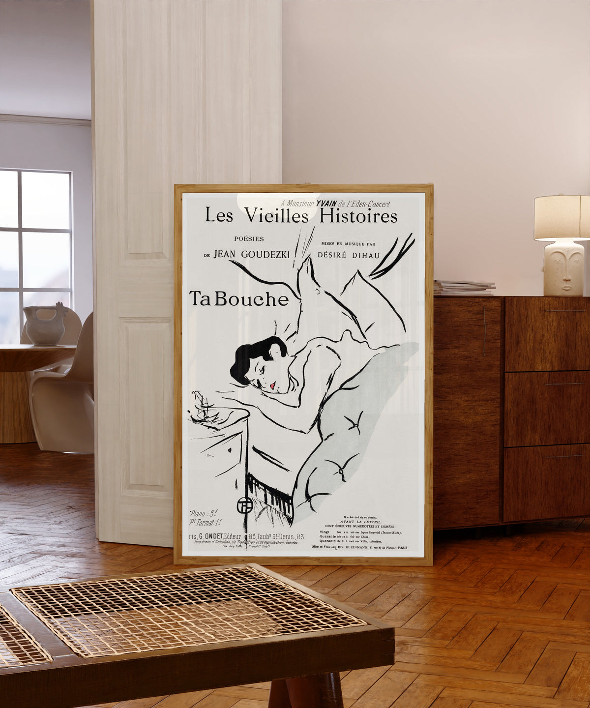 Framed art print of Ta Bouche by Henri de Toulouse-Lautrec, in a light wood frame leaning in a warm room with a parquet floor