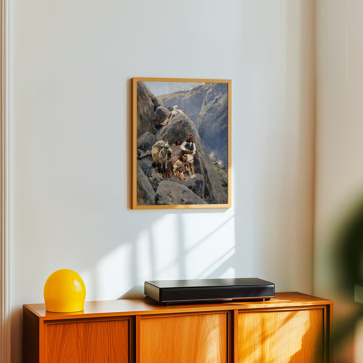 Framed art print of Apache Indians in the Mountains by Henry Farny, in a light wood frame on a white wall above an orange sideboard
