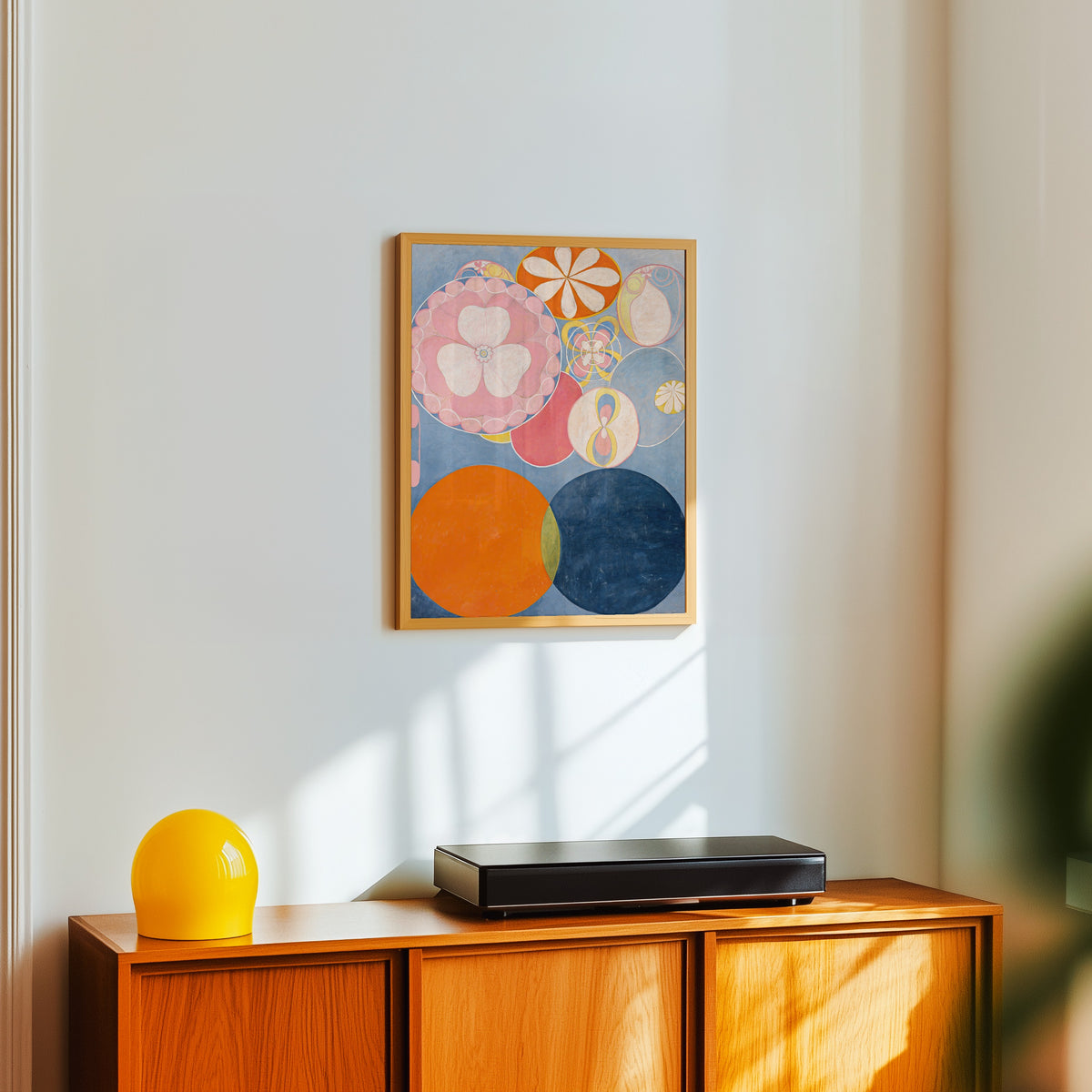 Framed art print of The Ten Largest, No. 2, Childhood by Hilma af Klint, in a light wood frame on a white wall above an orange sideboard