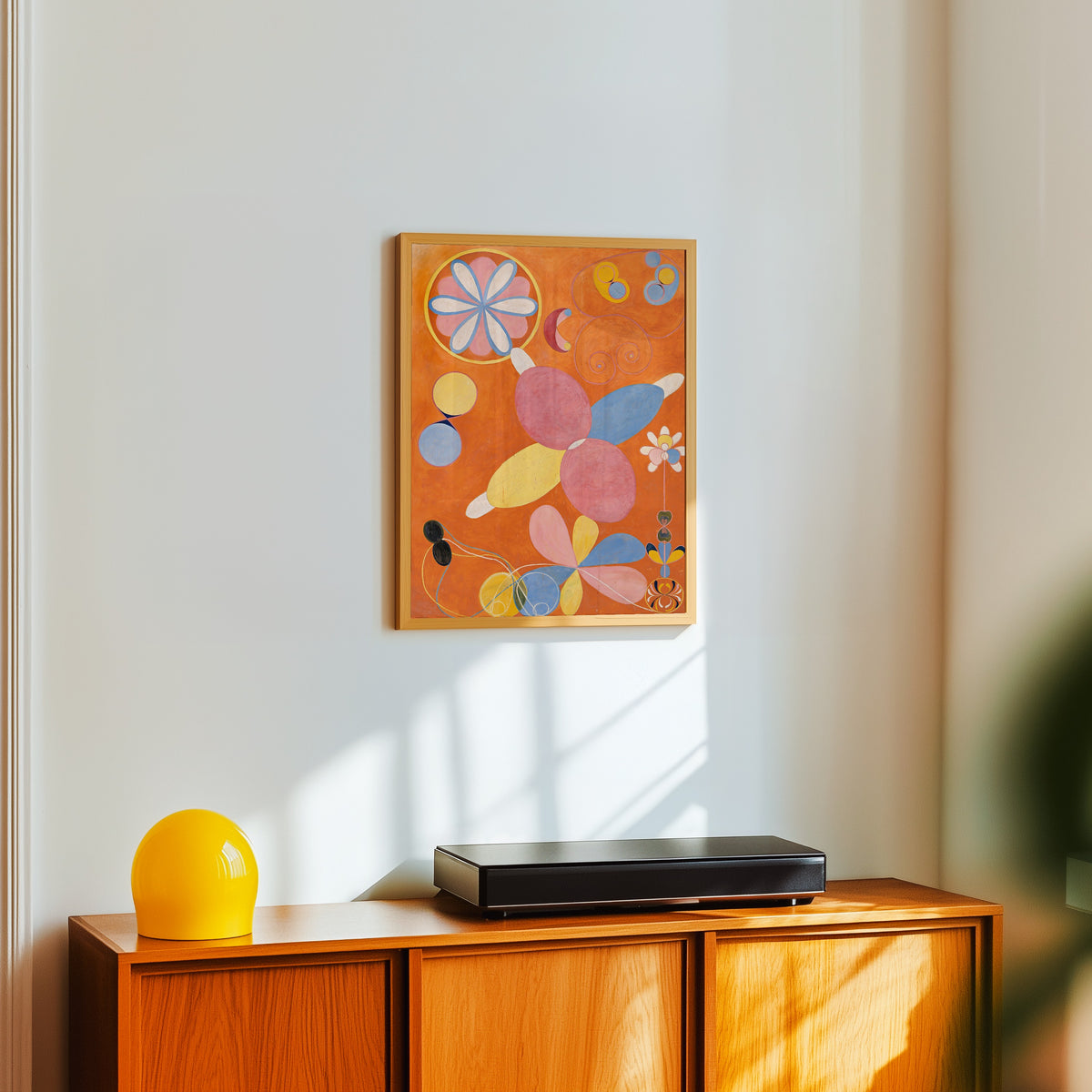 Framed art print of The Ten Largest, No. 4, Youth by Hilma af Klint, in a light wood frame on a white wall above an orange sideboard