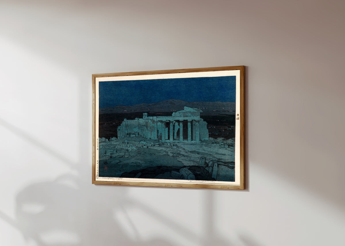 Framed art print of Ancient Ruins of Athens by Hiroshi Yoshida, in a light wood frame on a sunlit white wall, seen at a slight angle