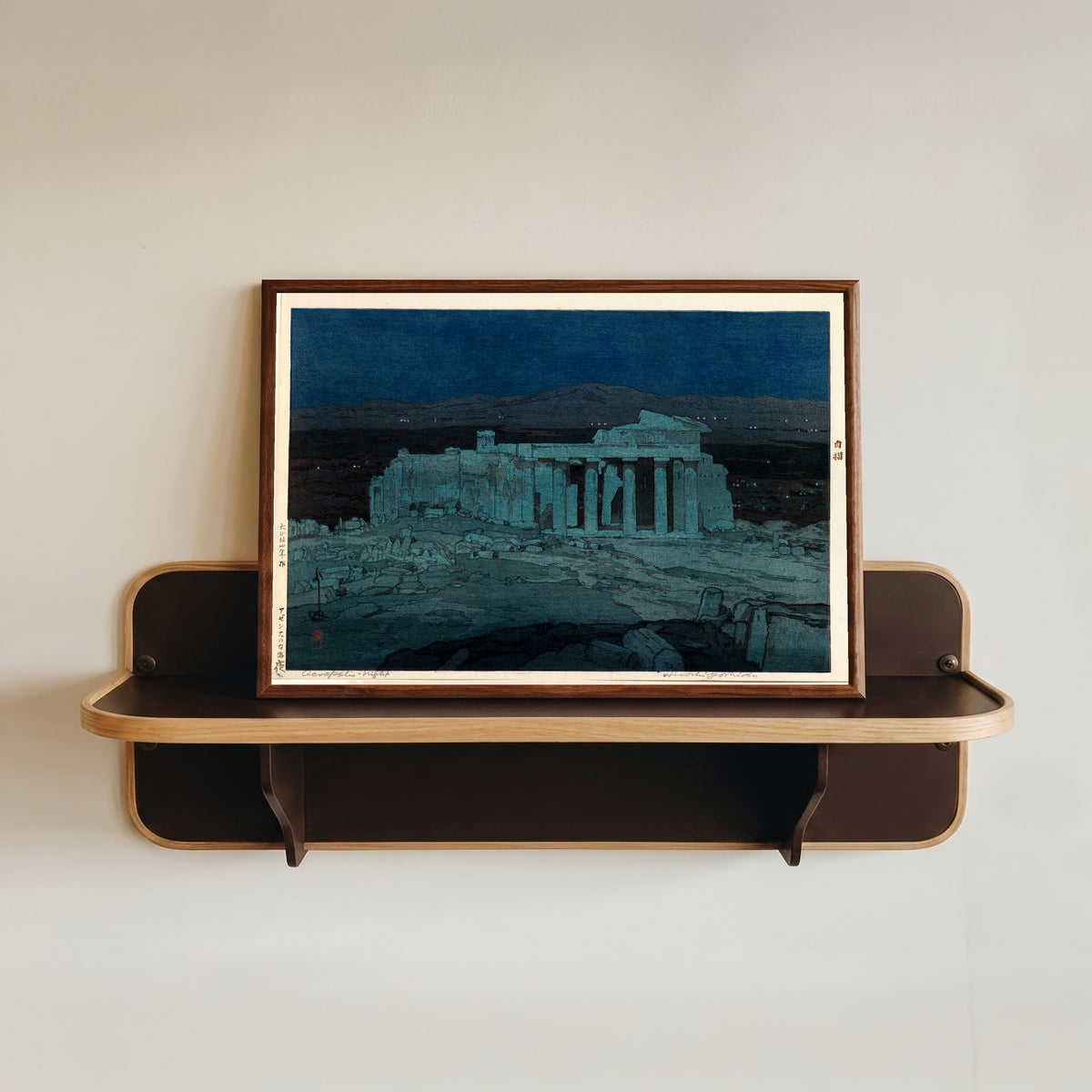 Framed art print of Ancient Ruins of Athens by Hiroshi Yoshida, in a dark wood frame resting on a wall shelf