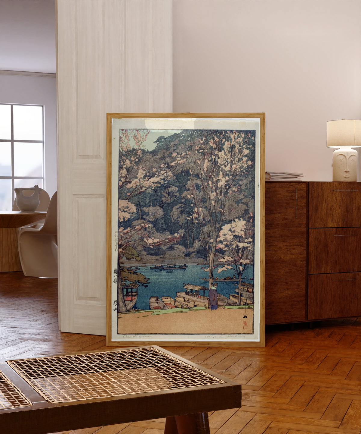 Framed art print of Arashiyama Lake by Hiroshi Yoshida, in a light wood frame leaning in a warm room with a parquet floor