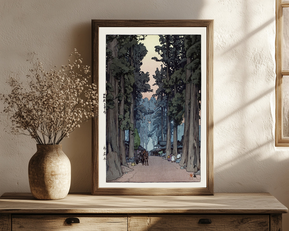 Framed art print of Cryptomeria Avenue by Hiroshi Yoshida, in a dark wood frame leaning on a rustic console beside dried flowers