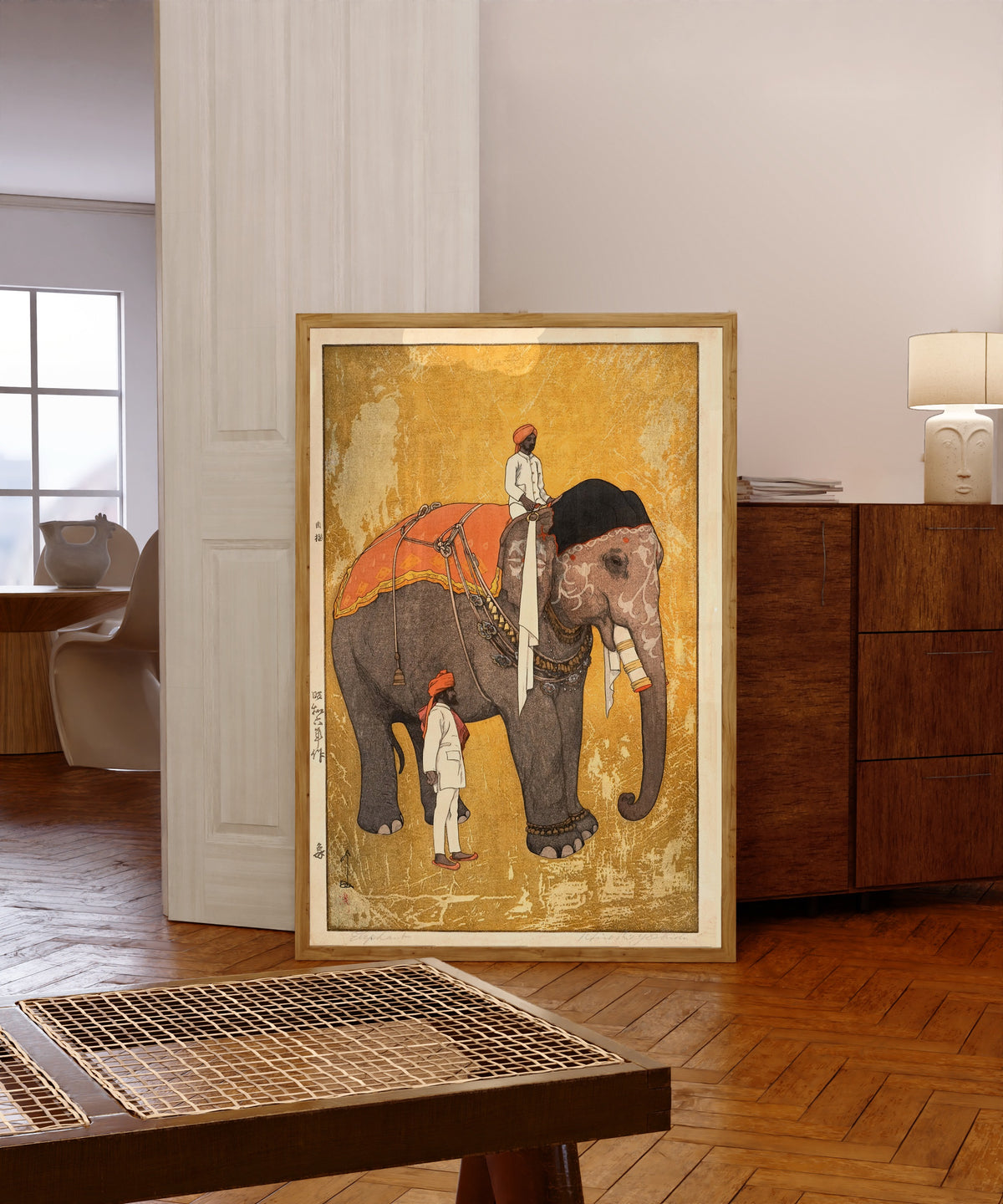 Framed art print of Elephant and Rider by Hiroshi Yoshida, in a light wood frame leaning in a warm room with a parquet floor