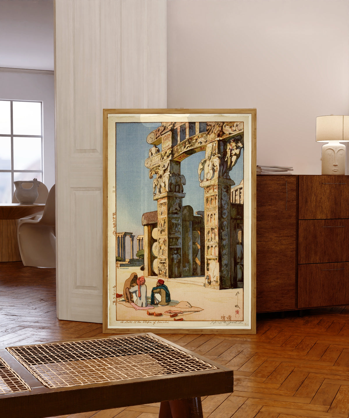 Framed art print of Gate to the Stupa at Sanchi, India by Hiroshi Yoshida, in a light wood frame leaning in a warm room with a parquet floor
