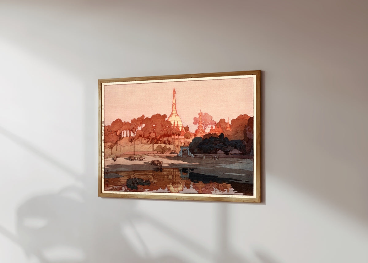 Framed art print of Golden Pagoda in Rangoon by Hiroshi Yoshida, in a light wood frame on a sunlit white wall, seen at a slight angle