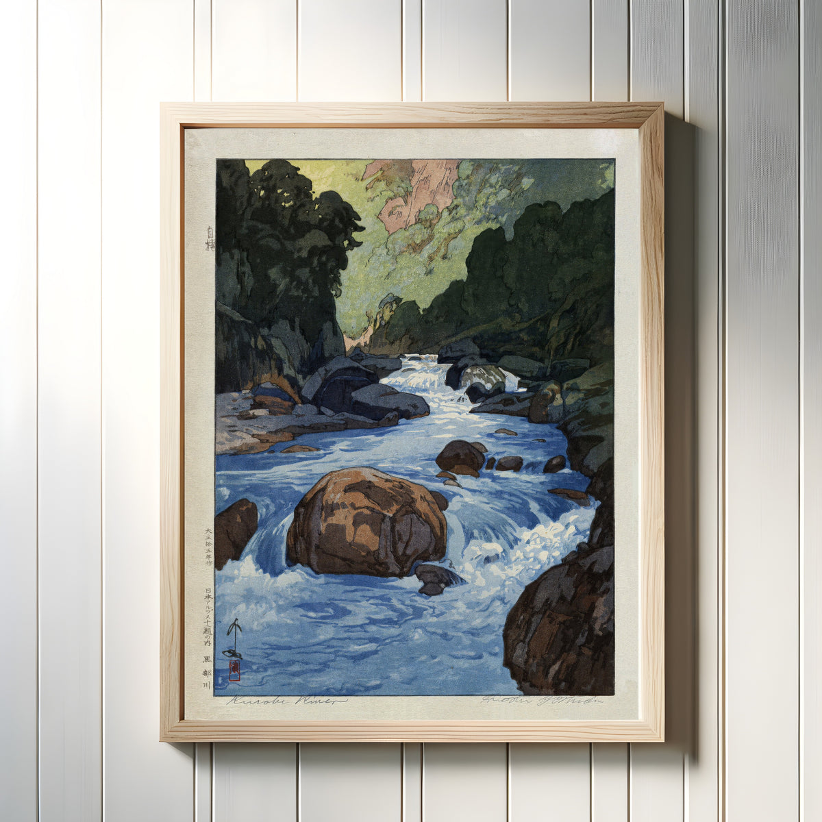 Framed art print of Kurobe River by Hiroshi Yoshida, in a light wood frame on a white panelled wall