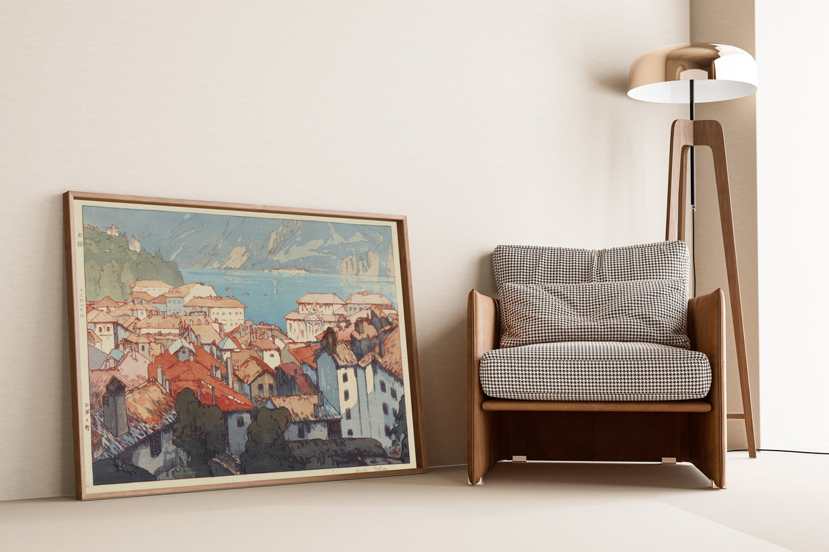 Framed art print of Lugano by Hiroshi Yoshida, leaning against a wall beside an armchair and a floor lamp