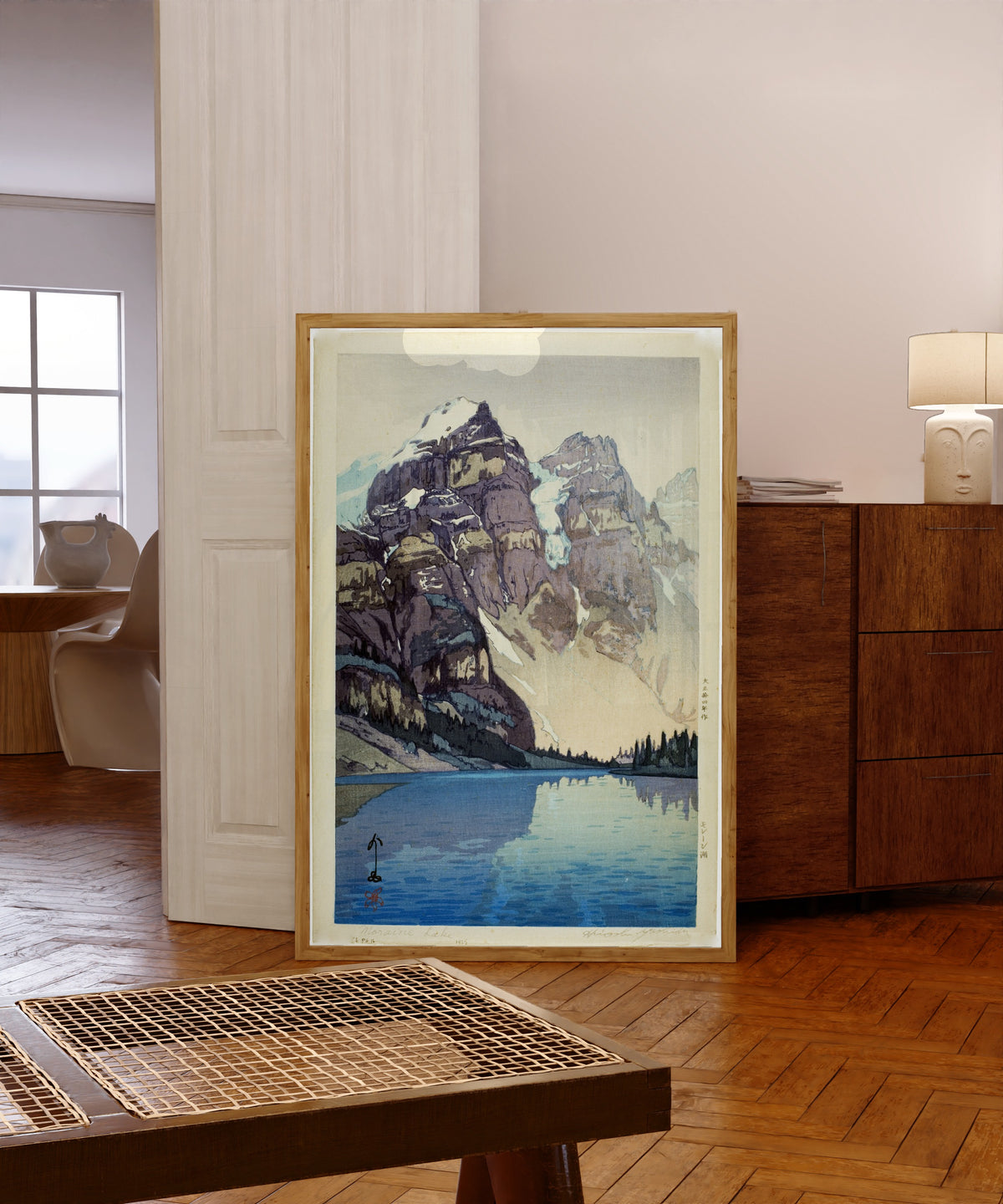 Framed art print of Moraine Lake by Hiroshi Yoshida, in a light wood frame leaning in a warm room with a parquet floor