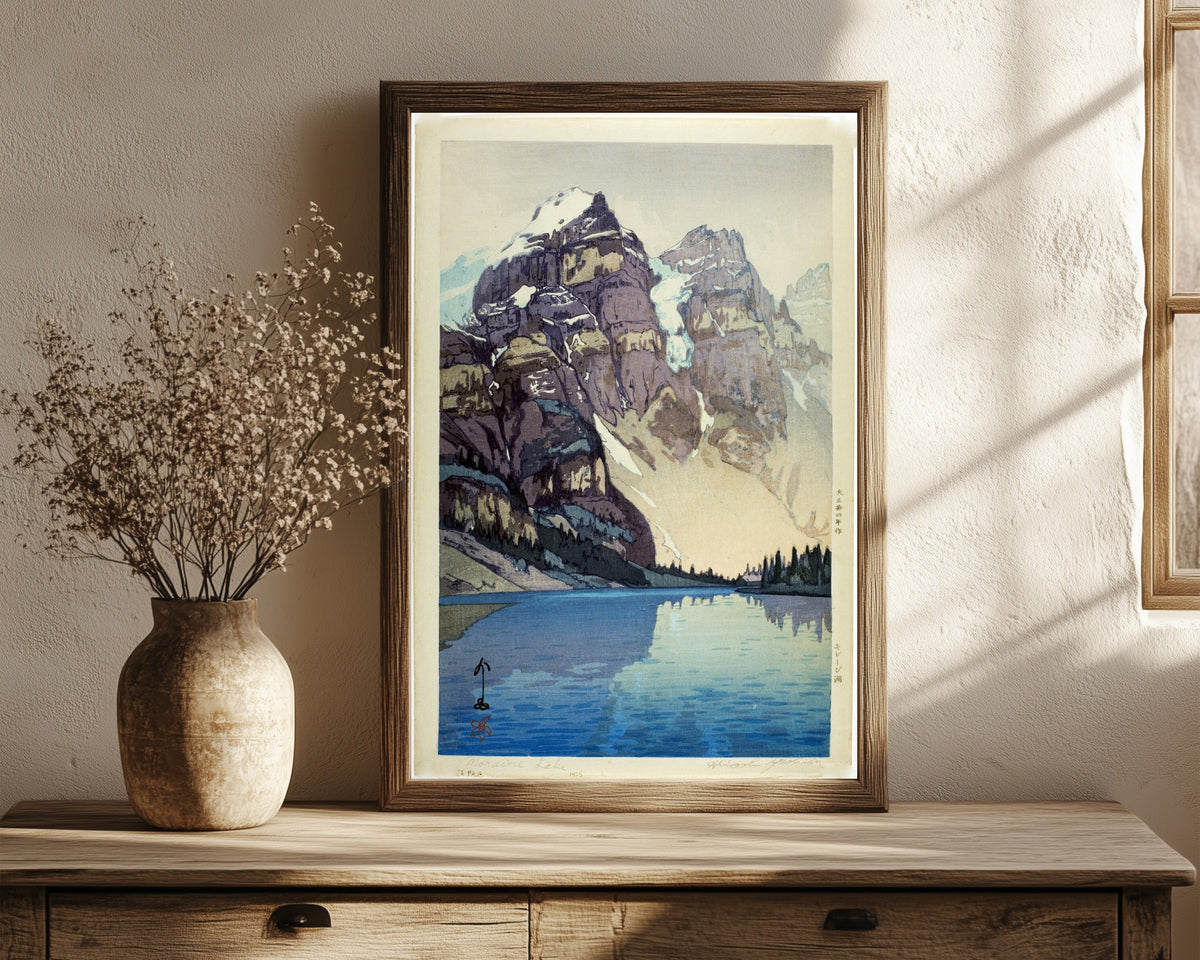 Framed art print of Moraine Lake by Hiroshi Yoshida, in a dark wood frame leaning on a rustic console beside dried flowers