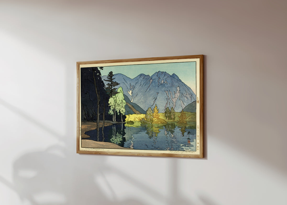 Framed art print of Mount Hodaka by Hiroshi Yoshida, in a light wood frame on a sunlit white wall, seen at a slight angle