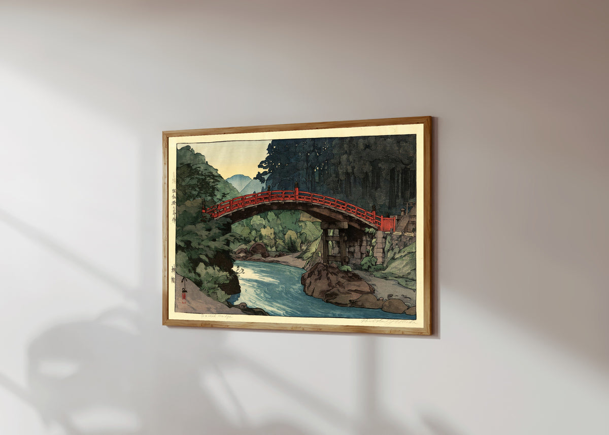 Framed art print of Sacred Bridge by Hiroshi Yoshida, in a light wood frame on a sunlit white wall, seen at a slight angle