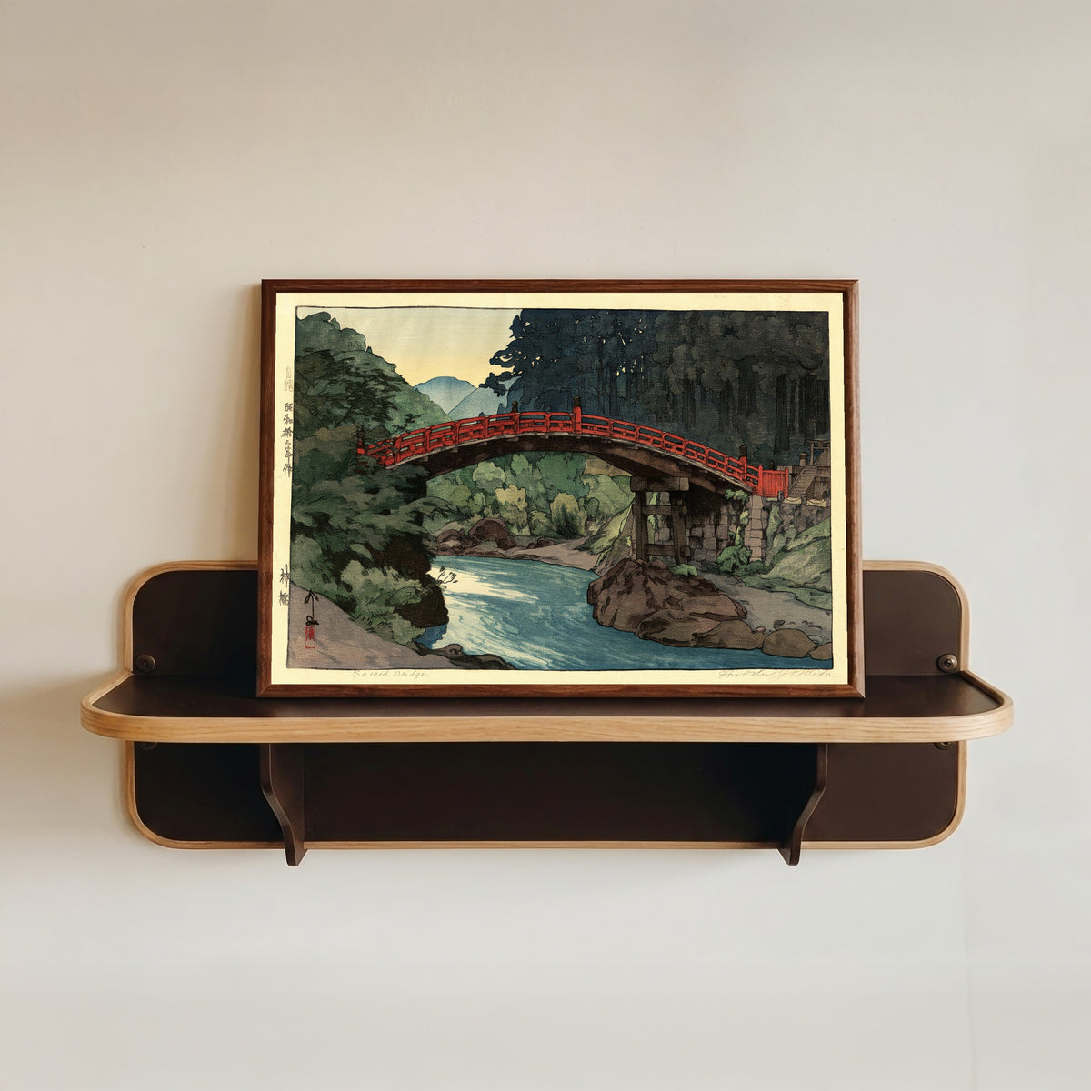 Framed art print of Sacred Bridge by Hiroshi Yoshida, in a dark wood frame resting on a wall shelf