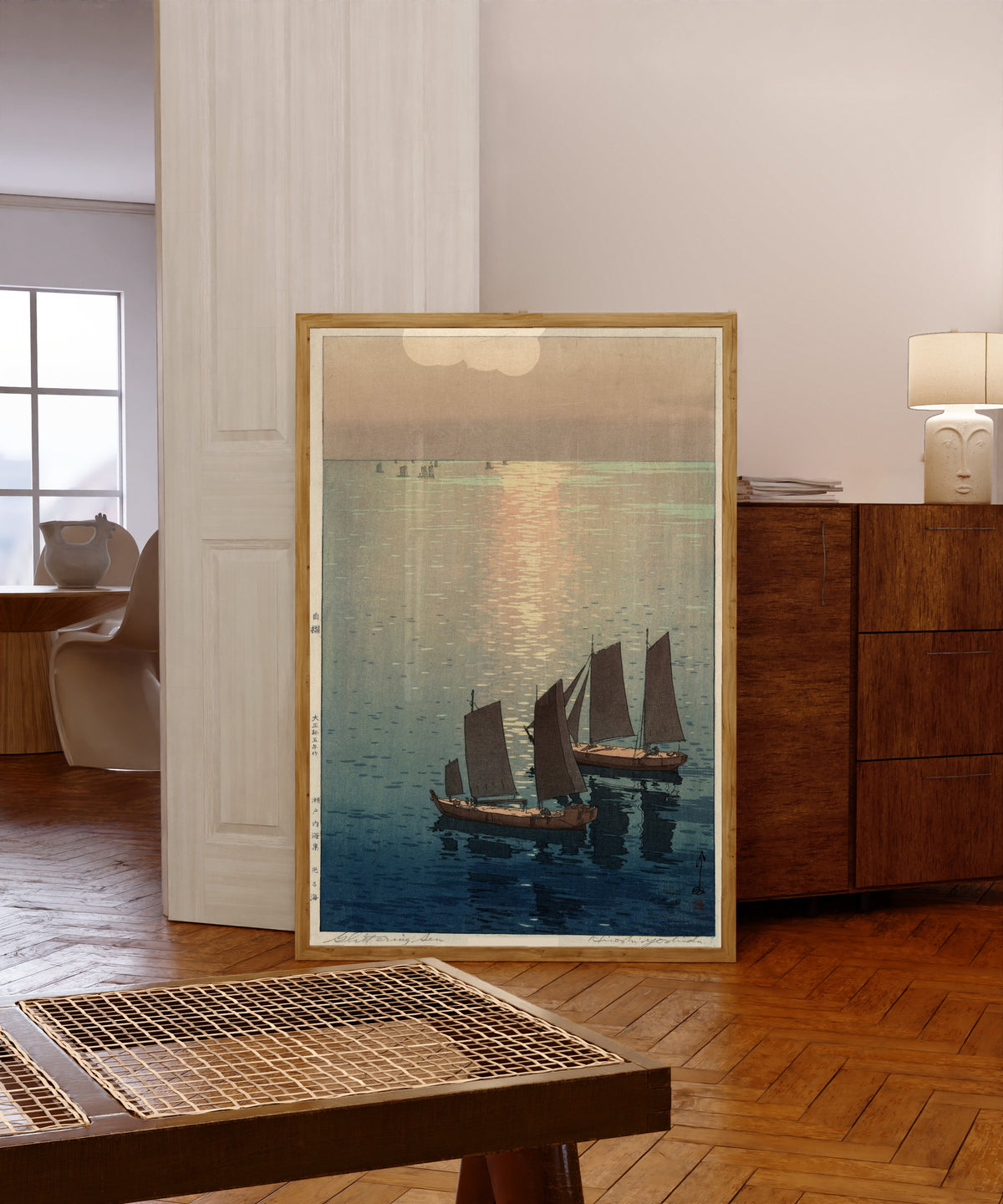 Framed art print of Afternoon Sailboats by Hiroshi Yoshida, in a light wood frame leaning in a warm room with a parquet floor