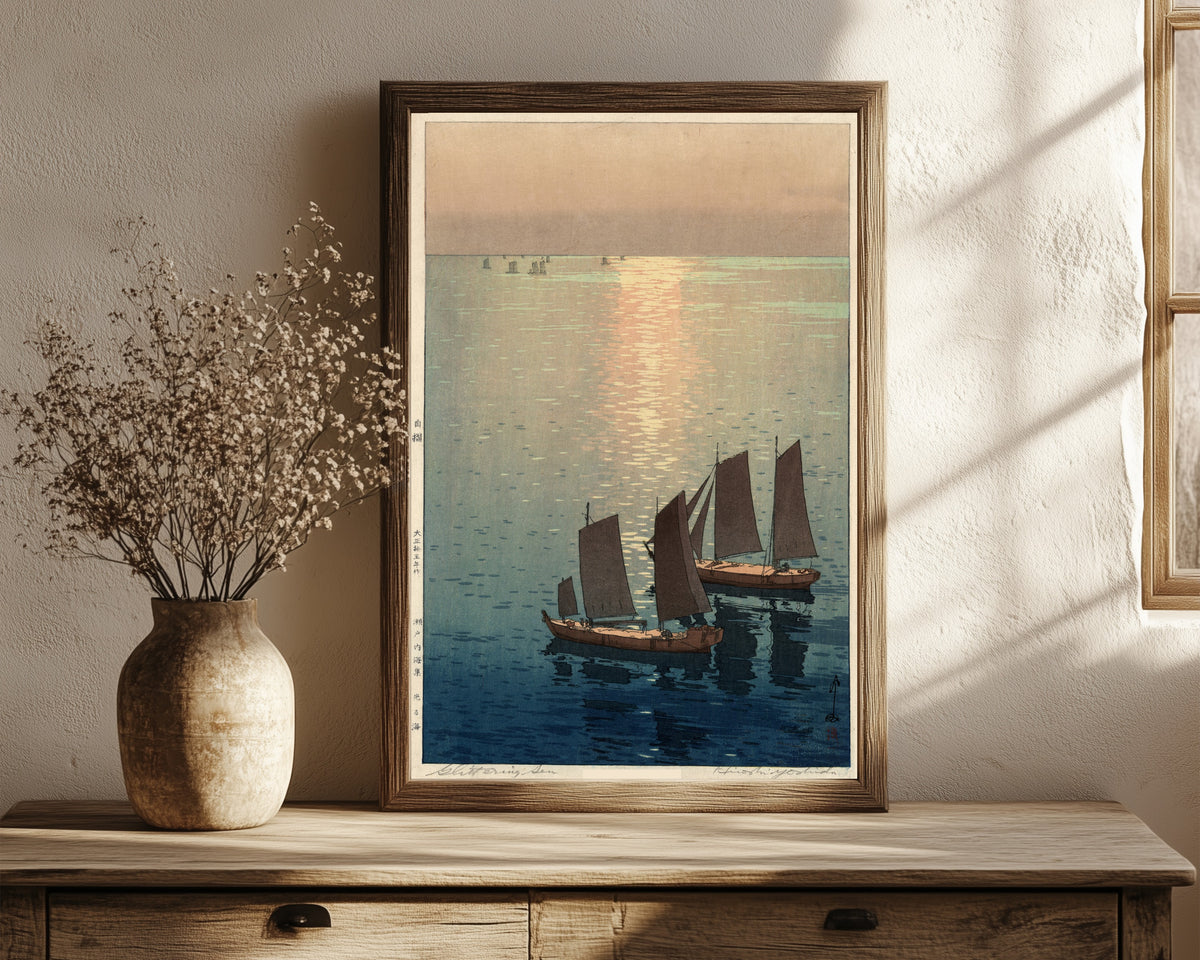 Framed art print of Afternoon Sailboats by Hiroshi Yoshida, in a dark wood frame leaning on a rustic console beside dried flowers
