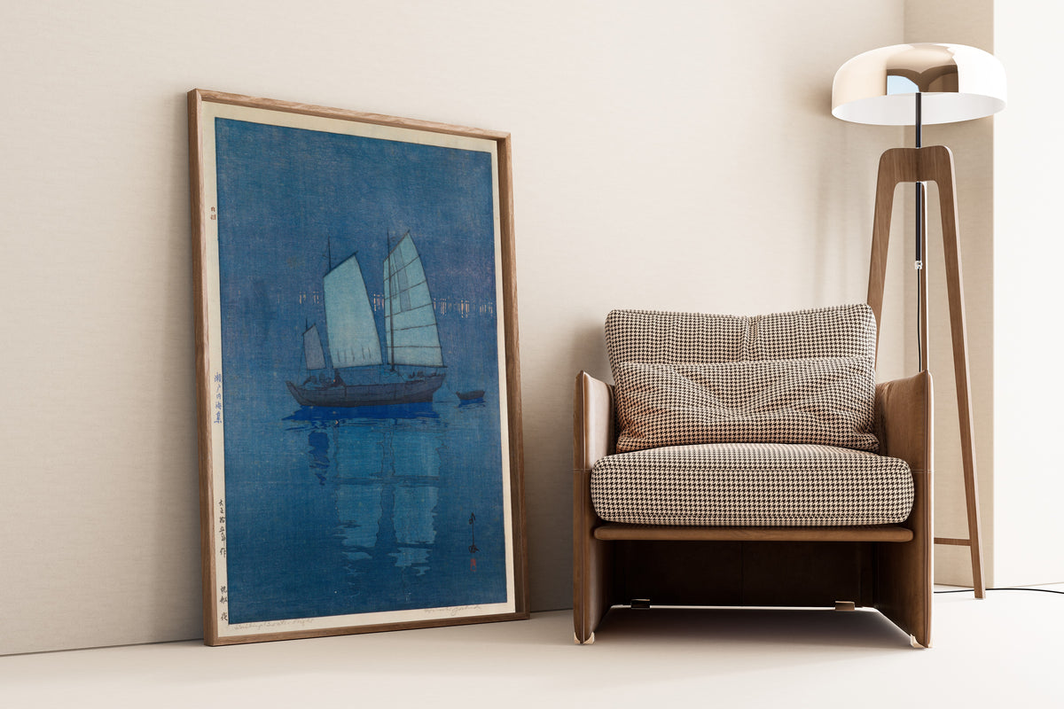 Framed art print of Sailing Boats, Night by Hiroshi Yoshida, leaning against a wall beside an armchair and a floor lamp