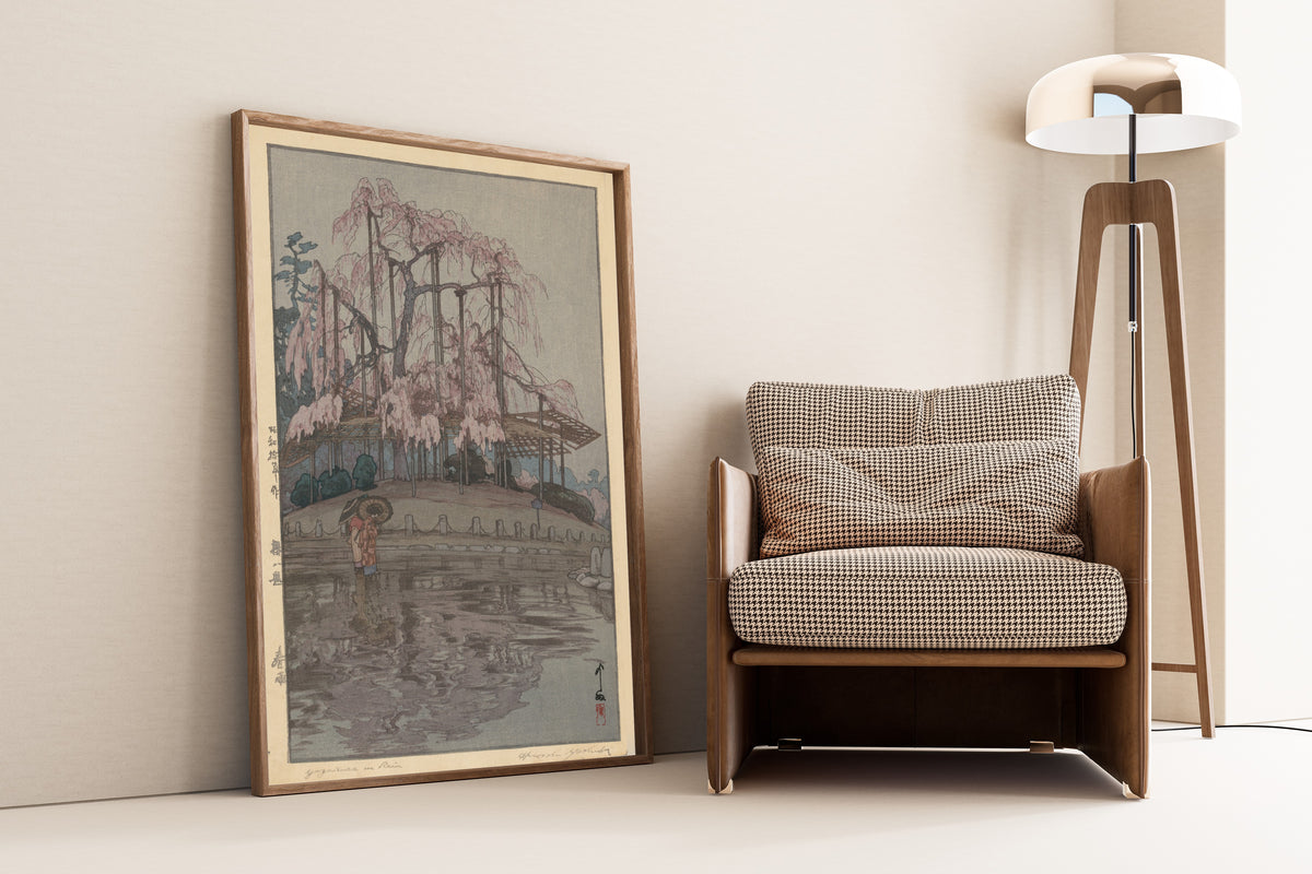 Framed art print of Spring Rain, from Eight Scenes of Cherry Blossoms by Hiroshi Yoshida, leaning against a wall beside an armchair and a floor lamp