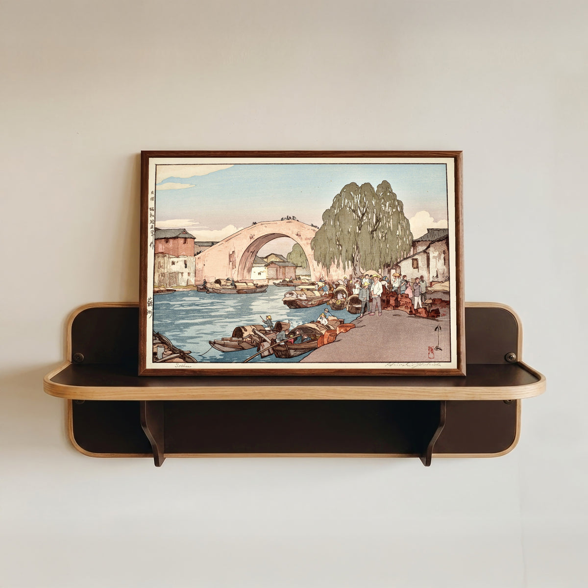 Framed art print of Suzhou by Hiroshi Yoshida, in a dark wood frame resting on a wall shelf