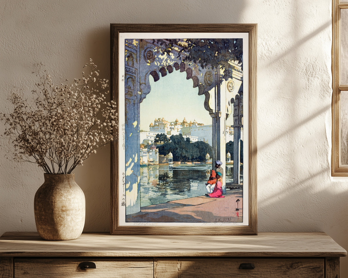 Framed art print of Udaipur Castle, India by Hiroshi Yoshida, in a dark wood frame leaning on a rustic console beside dried flowers