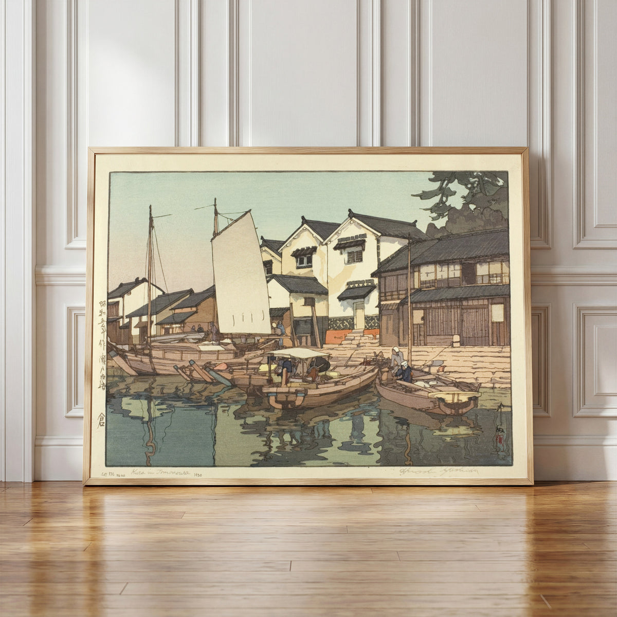 Framed art print of Tomonoura Warehouse by Hiroshi Yoshida, in a light wood frame leaning against a panelled white wall