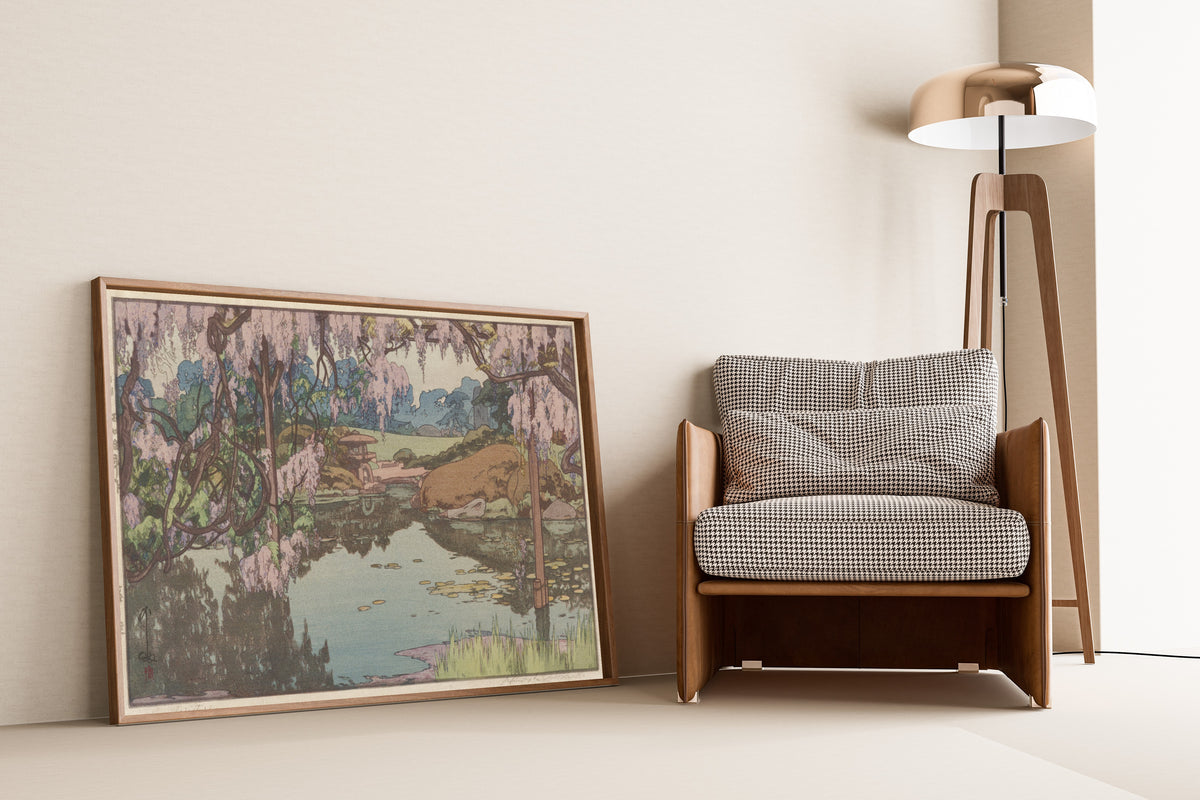 Framed art print of Wisteria Garden by Hiroshi Yoshida, leaning against a wall beside an armchair and a floor lamp