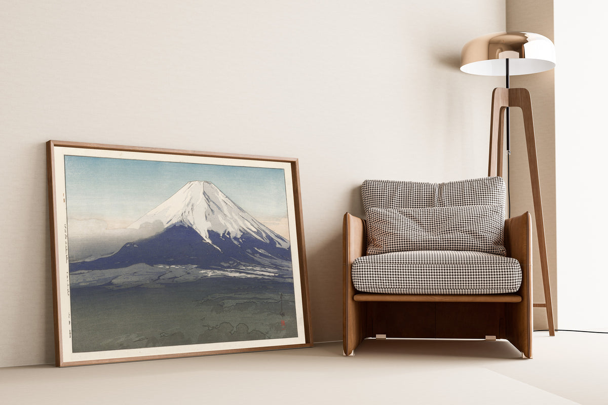 Framed art print of Yoshida Village by Hiroshi Yoshida, leaning against a wall beside an armchair and a floor lamp