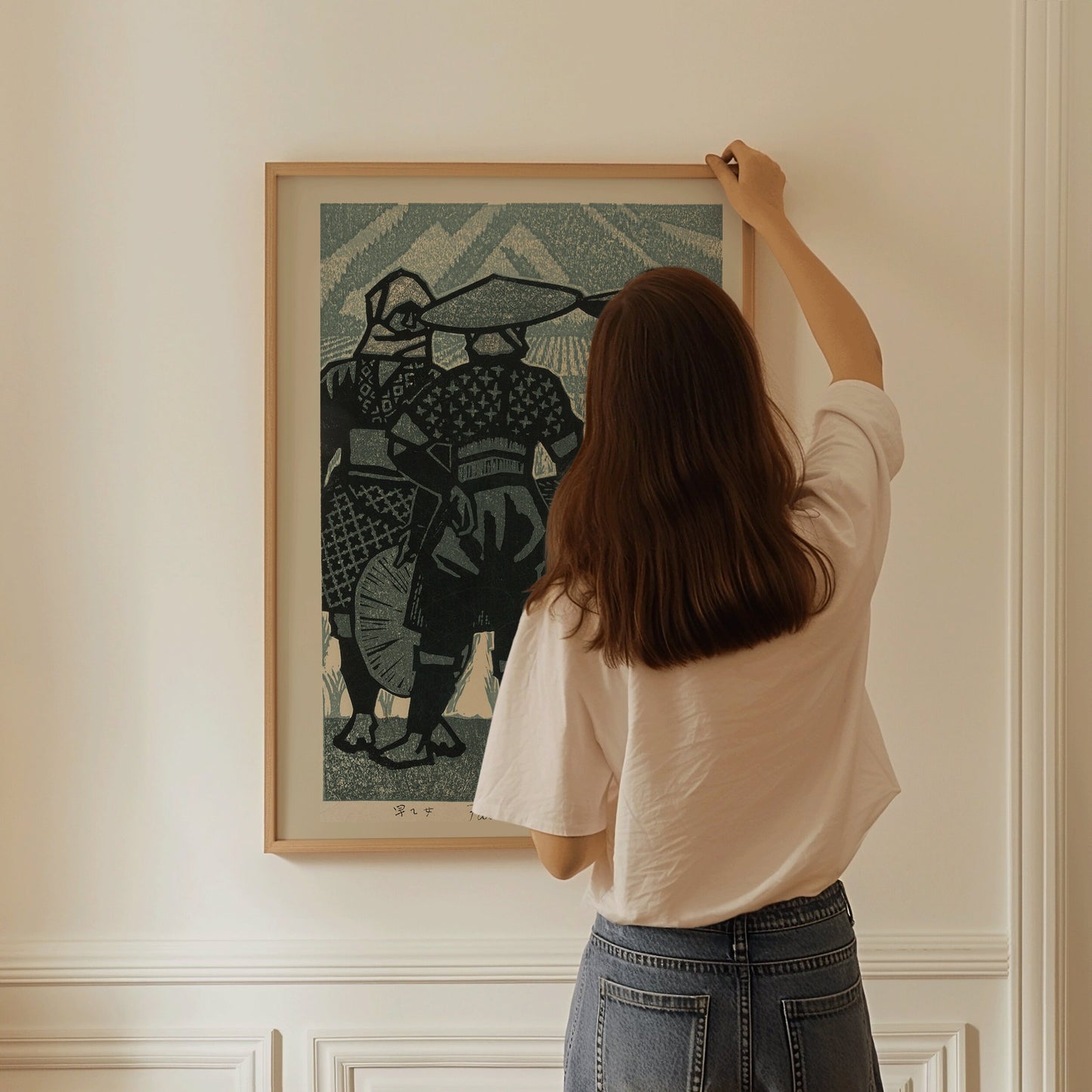 Woman hanging Shiro Kasamatsu's "Farmer's Daughters" framed vintage Japanese woodblock art in blue on a wall.