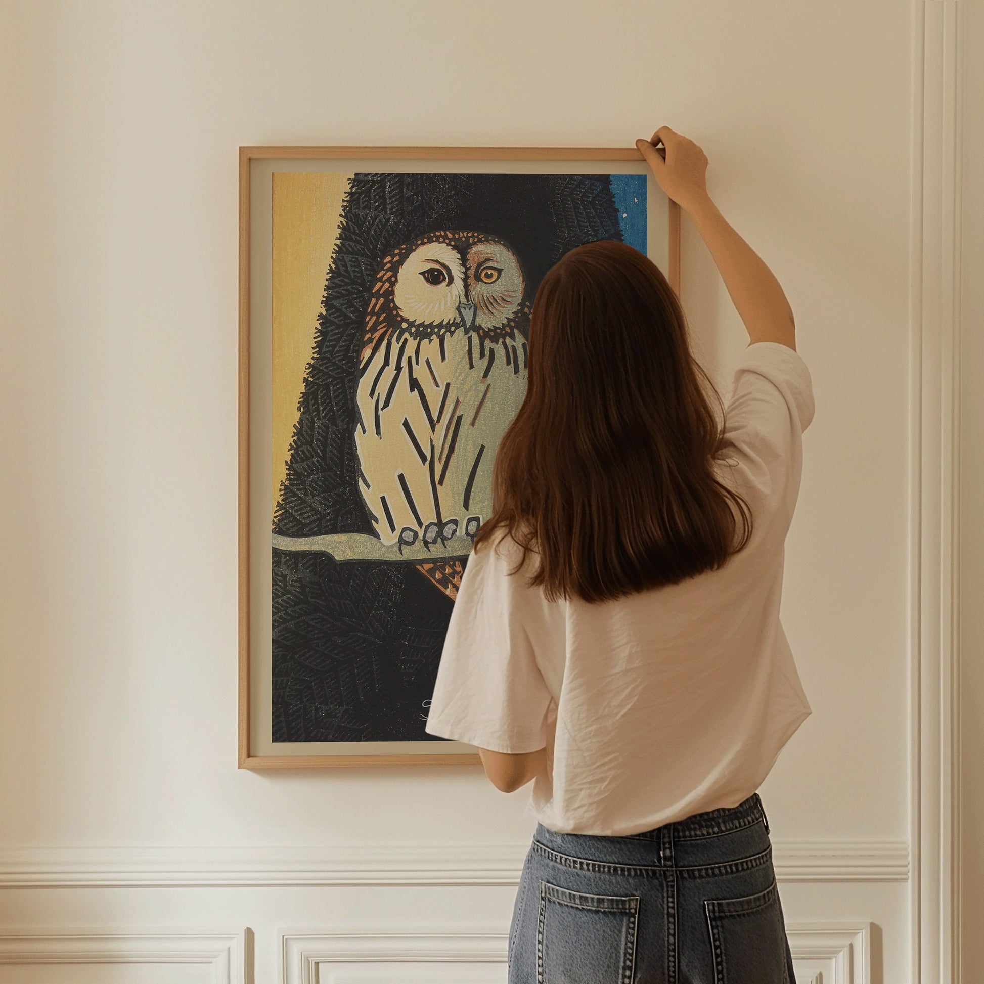 Person hanging Shiro Kasamatsu's vintage Japanese owl woodblock art in blue, available framed in bespoke or classic styles.