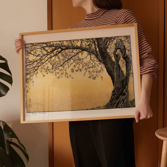 Toshi Yoshida Cherry Blossoms art print in yellow gold frame held by person, showcasing vintage Japanese woodblock craftsmanship.