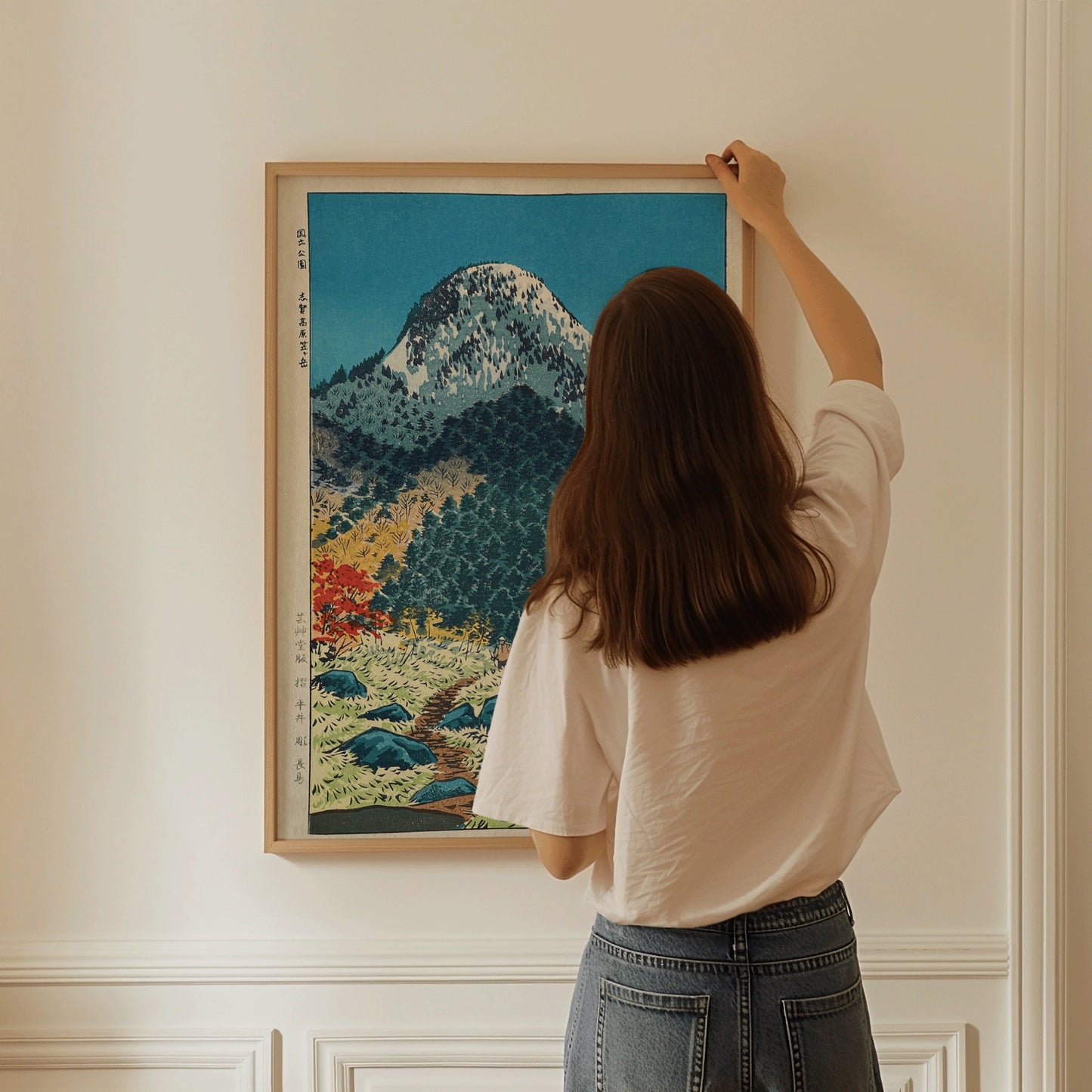 Person hanging framed Shiro Kasamatsu art print of Mount Kasugatake, museum-quality Shin-Hanga style, in a minimalist room.