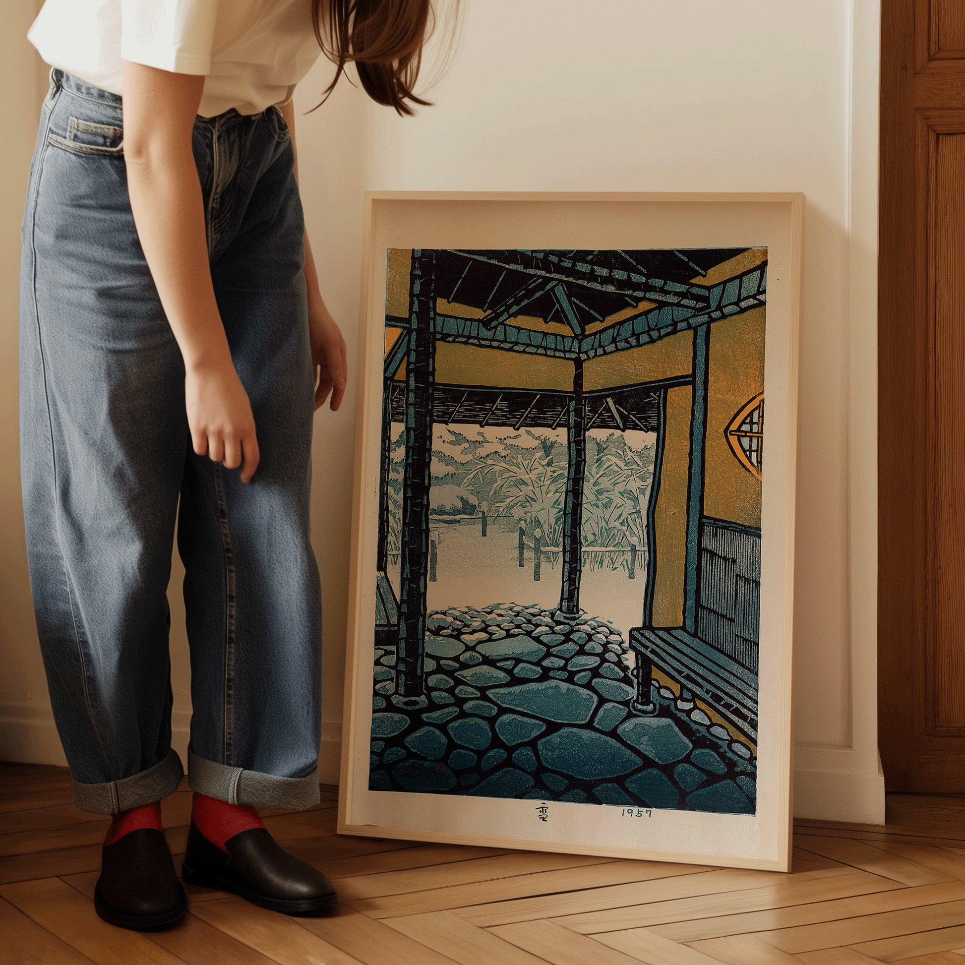 Woman admiring framed Shiro Kasamatsu "Snow" vintage Japanese woodblock art in green, enhancing home decor.