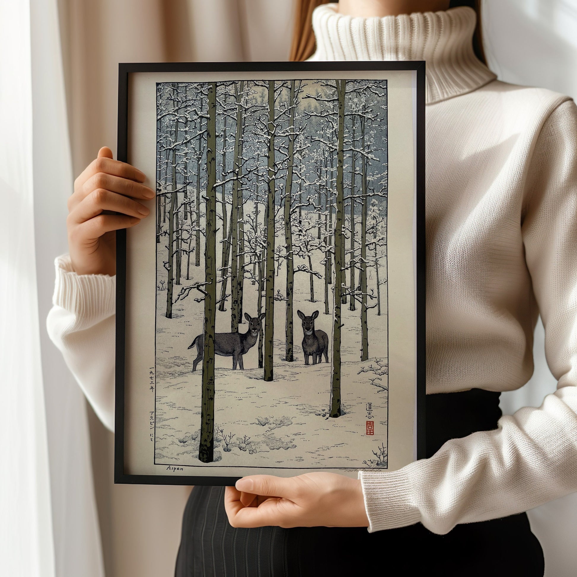 Woman holding Toshi Yoshida Aspen woodblock print framed in bespoke handcrafted frame, showcasing snow-covered forest scene.