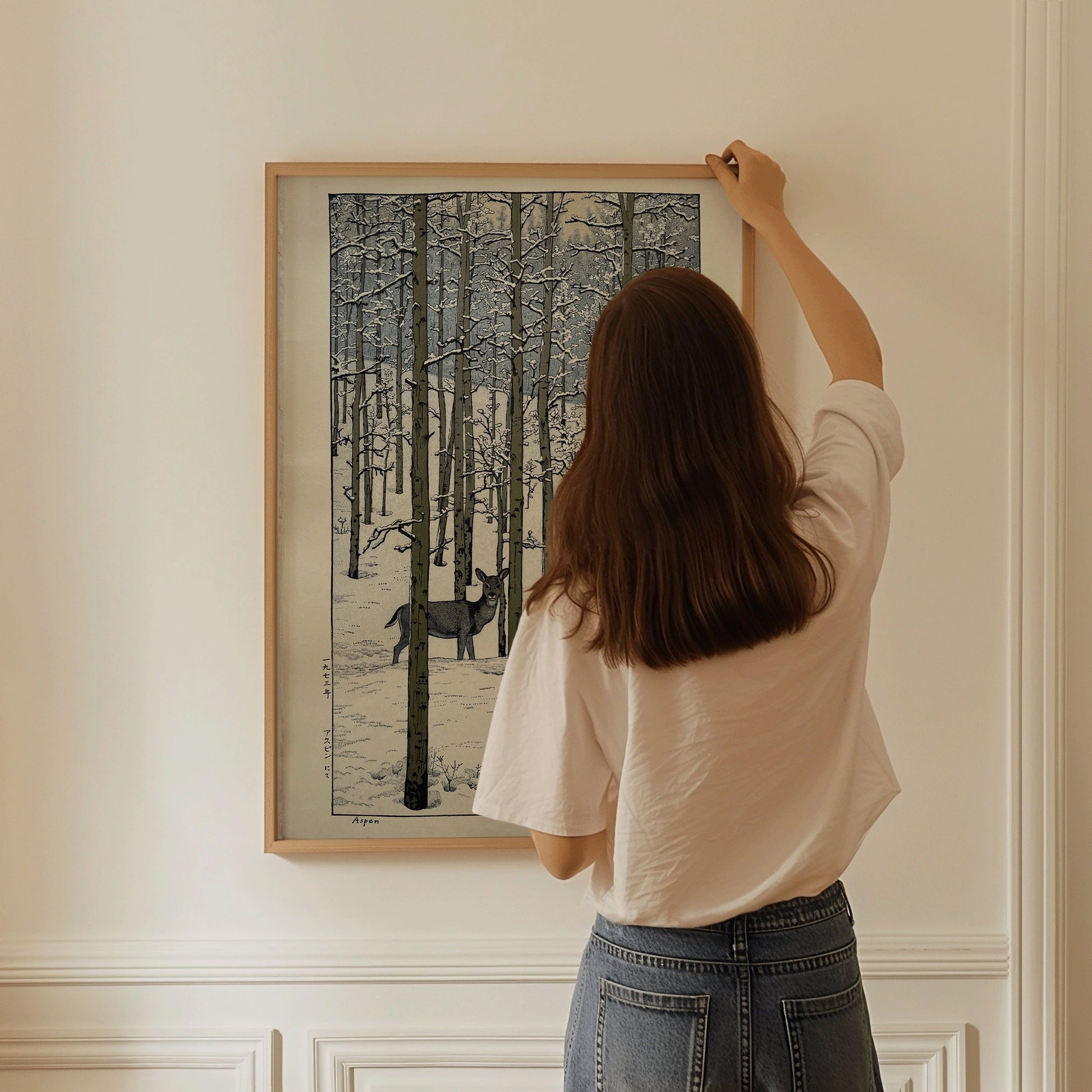 Woman hanging framed Toshi Yoshida Aspen art piece on wall