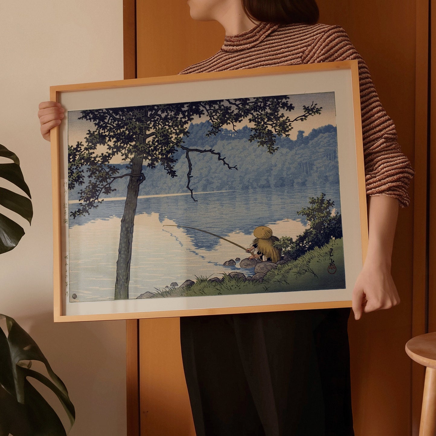 Person holding framed Kawase Hasui Lake Matsubura woodblock print in room.