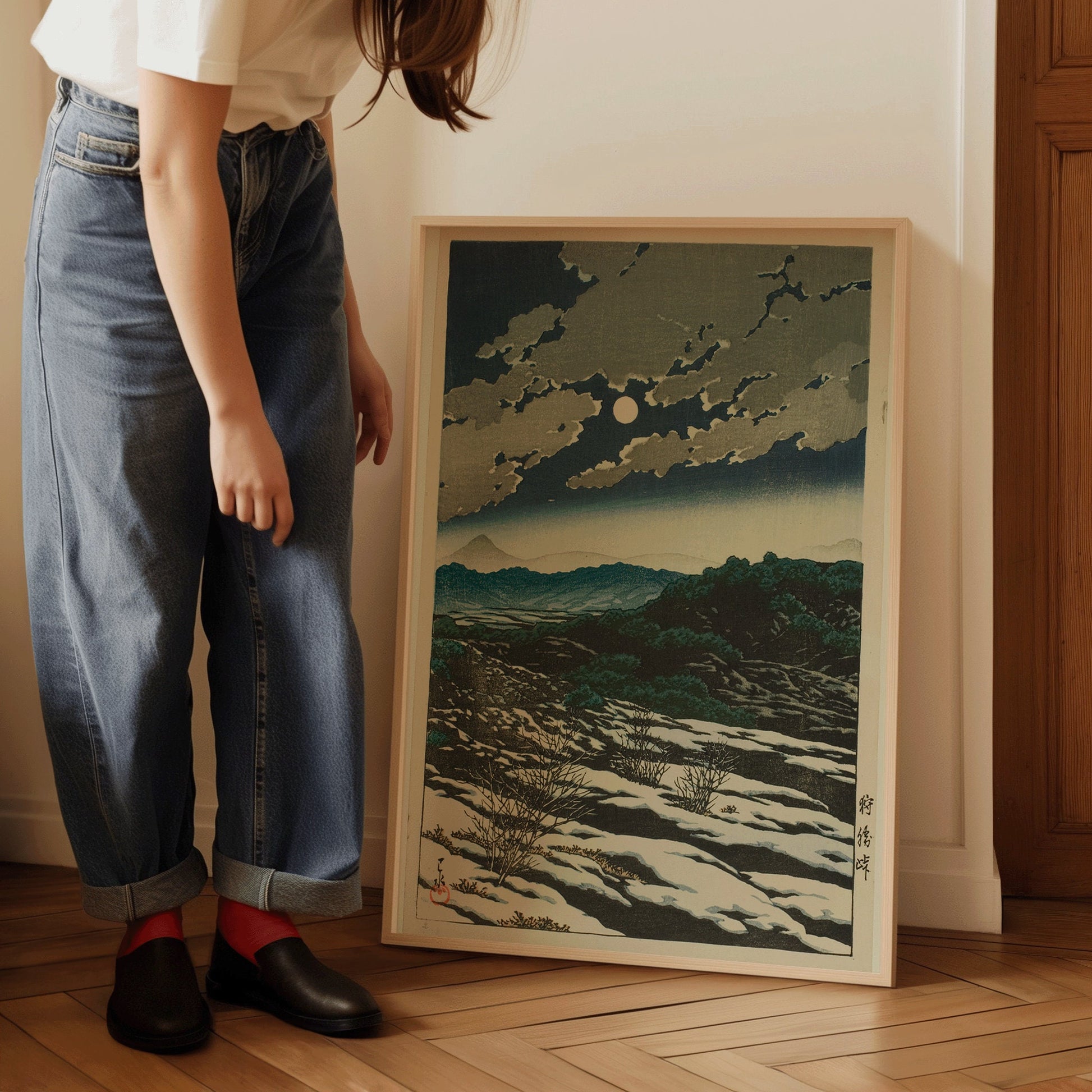 Person holding Kawase Hasui's Karikachi Mountain Pass art in a frame, vintage Japanese woodblock print displayed on a wooden floor.