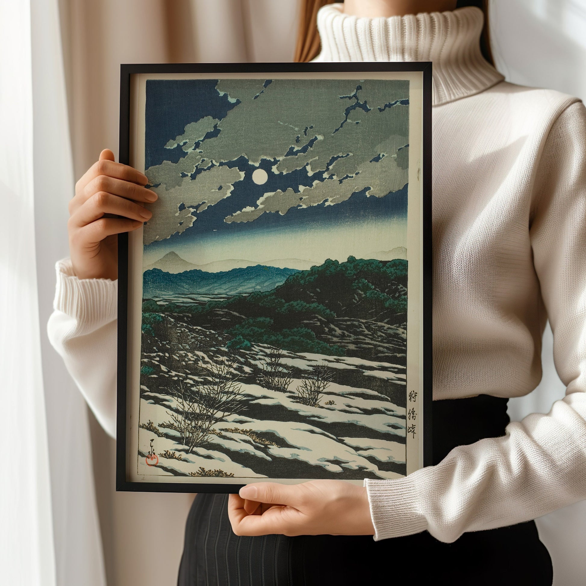 Woman holding framed Kawase Hasui Karikachi Mountain Pass woodblock art print, showcasing vintage Japanese design.