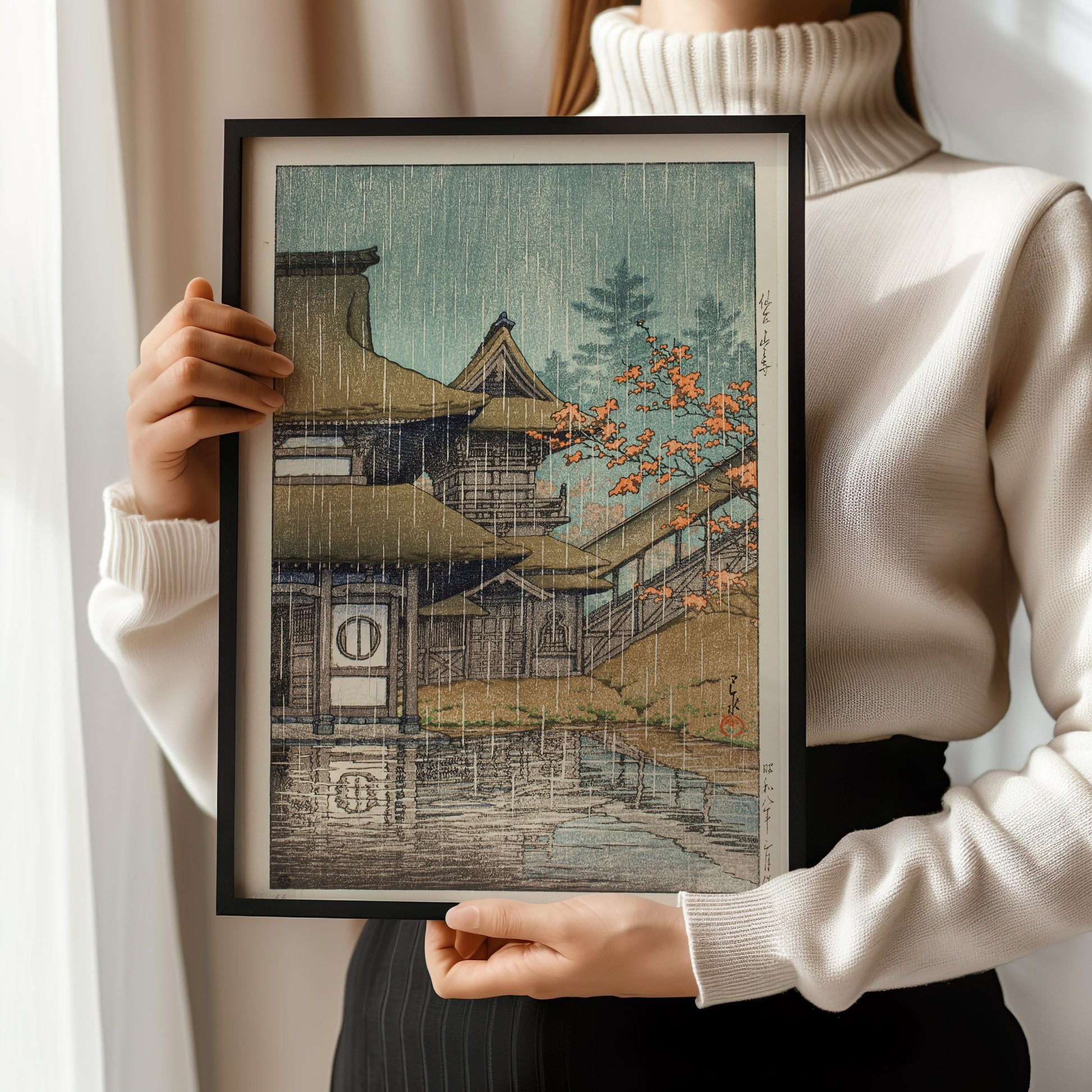 Woman holding framed Kawase Hasui Mountain Temple at Senzai woodblock print in a turtleneck sweater.