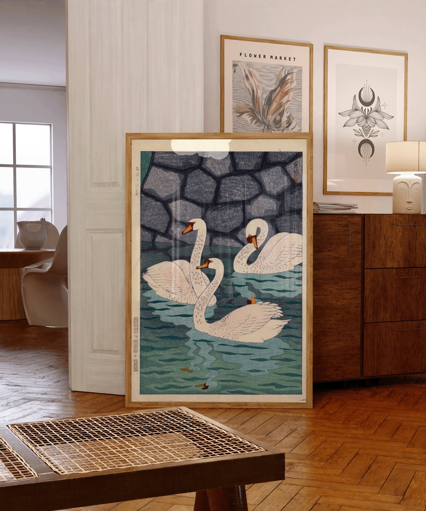 Framed vintage Japanese woodblock print with swans, showcased in a cozy room with wooden furniture and art-filled walls.