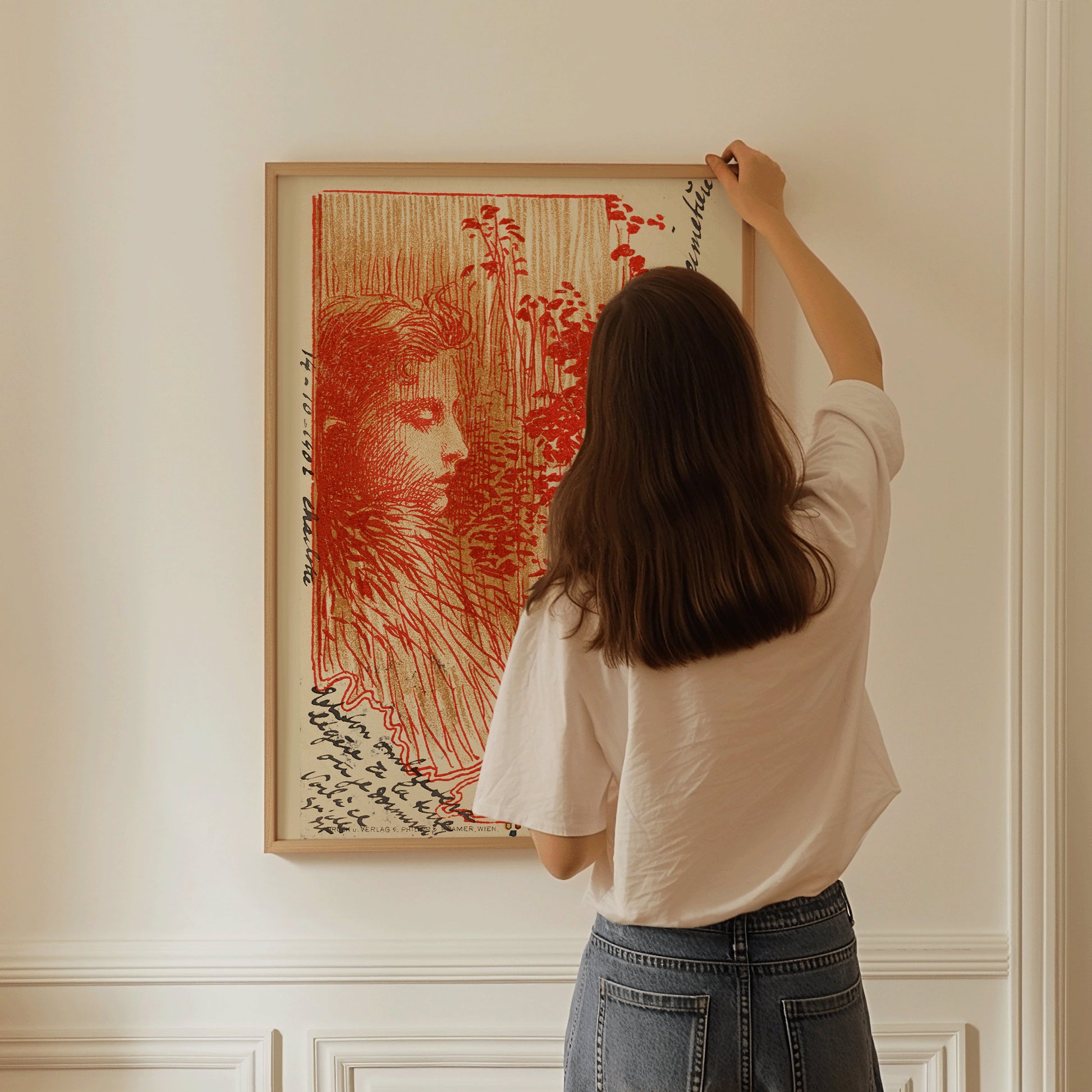 Woman hanging framed Koloman Moser vintage exhibition poster in red on a wall.