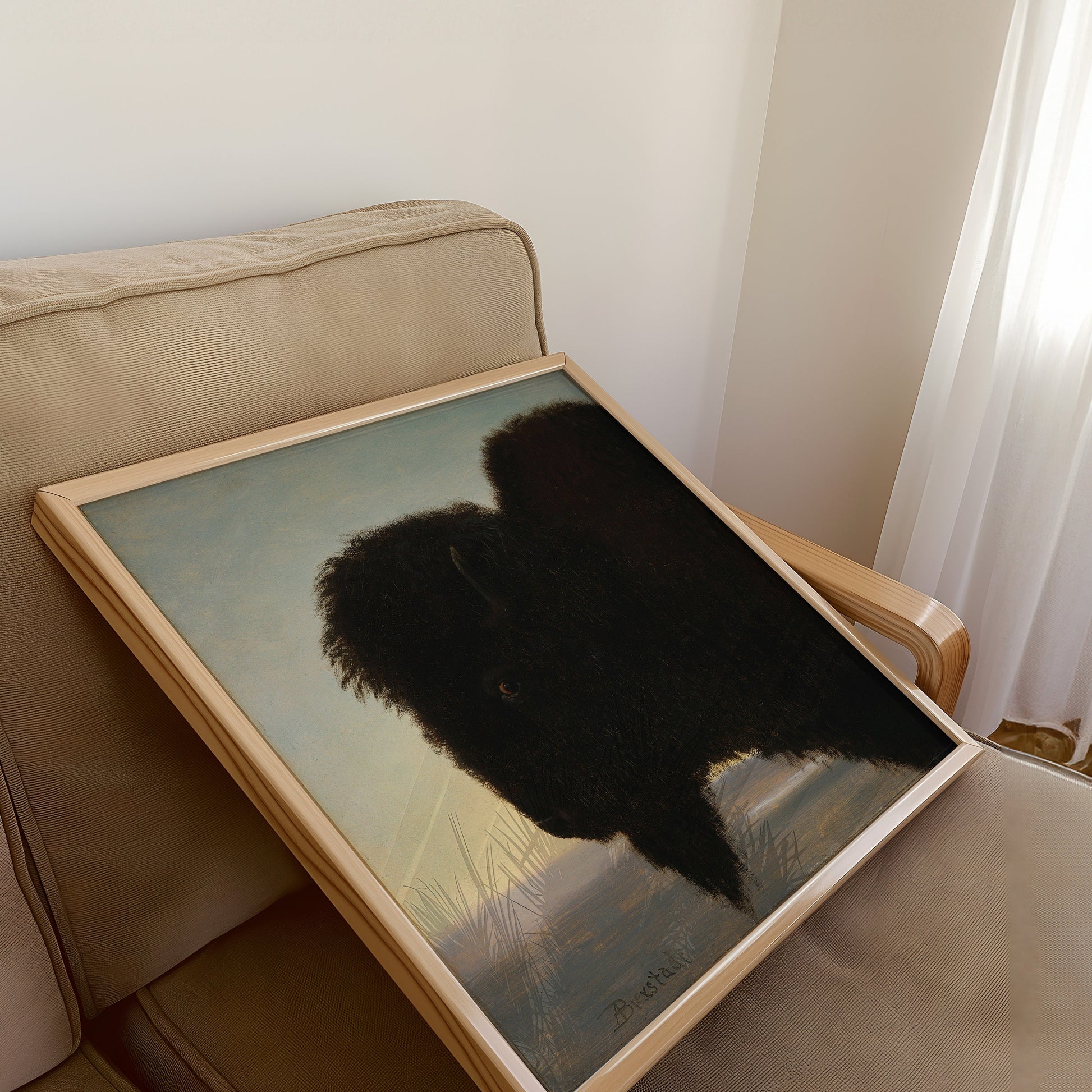 Framed buffalo painting resting on beige armchair in well-lit room