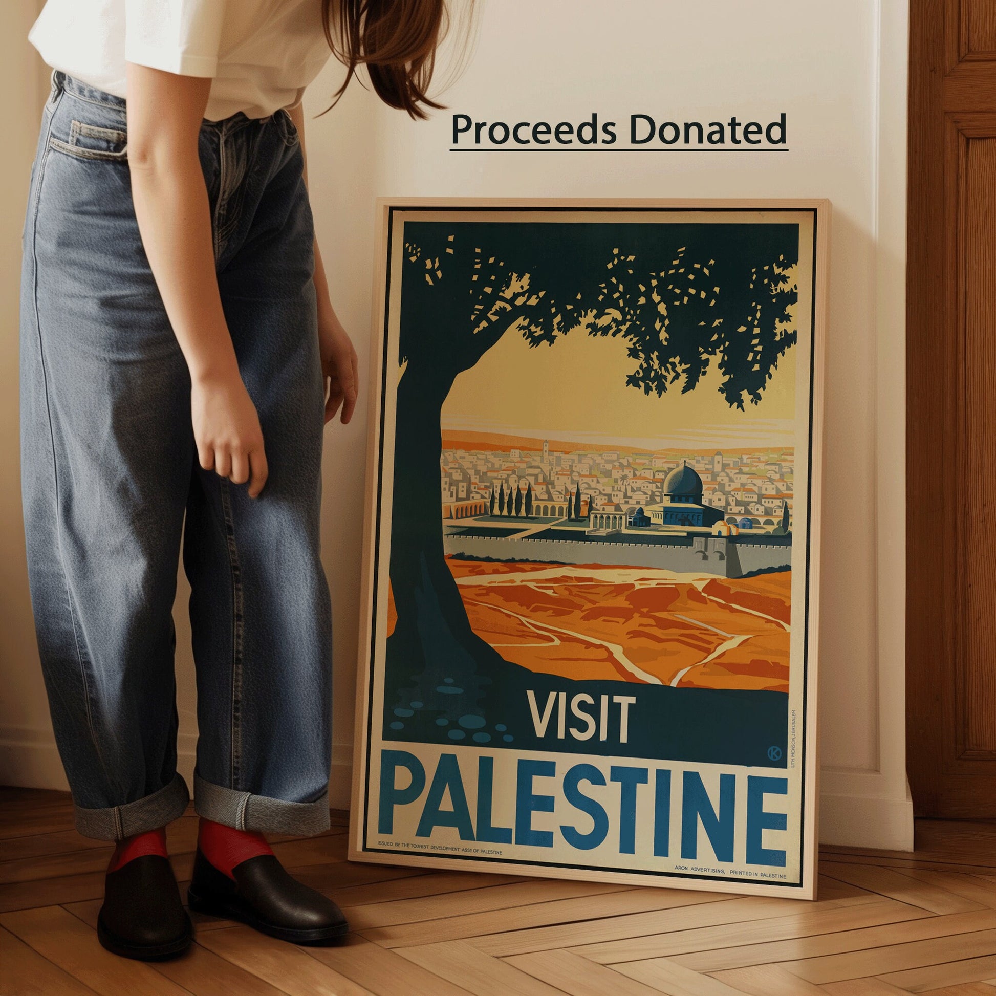 Vintage Visit Palestine poster with scenic view, framed, proceeds donated to Palestine Children's Relief Fund, leaning against wall.